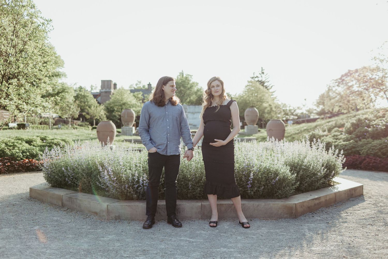 A couple stands in front of a landscaped garden area with stone walkways.