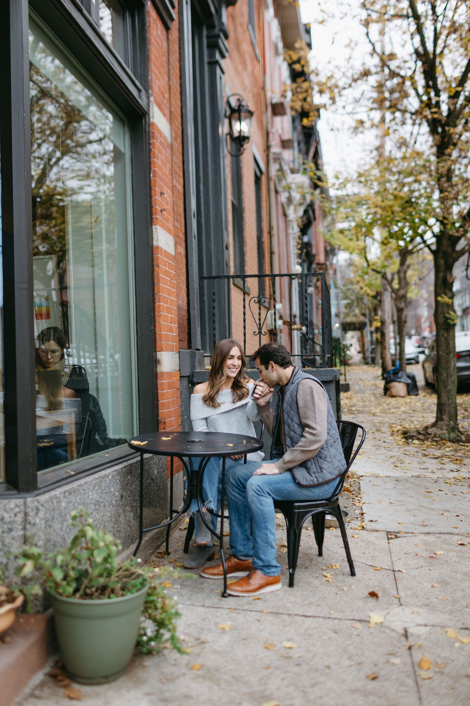 Couple enjoying coffee at outdoor cafe table on autumn city sidewalk.