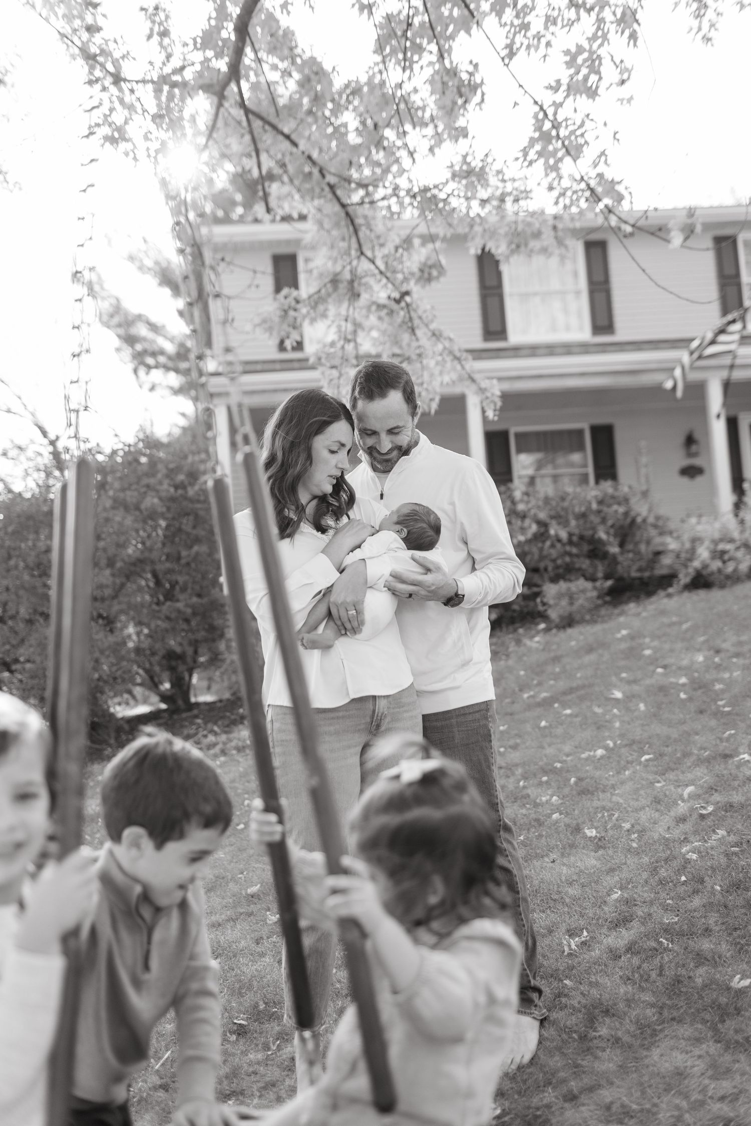 A family moment in a backyard with children playing on swings in the foreground.