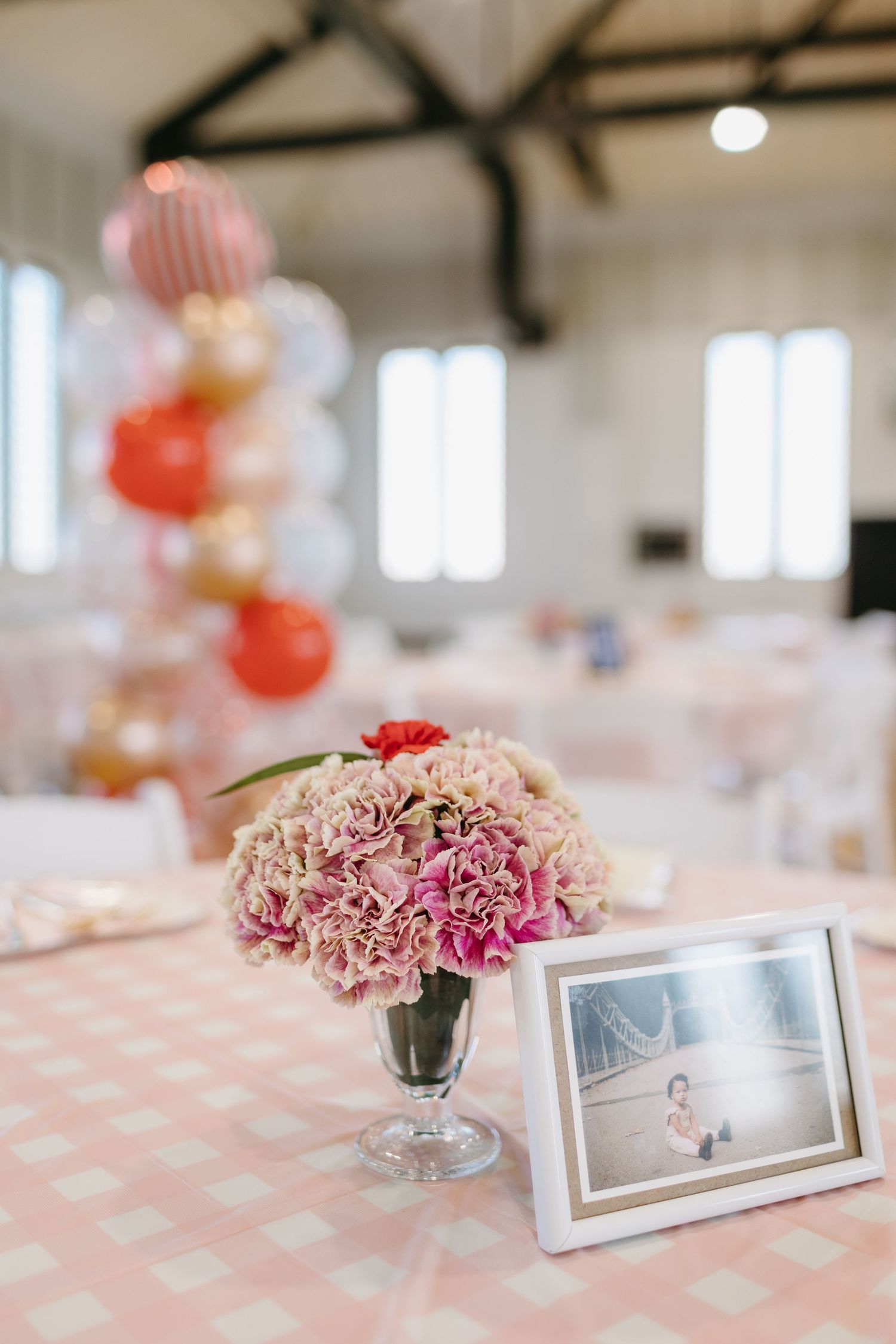 Pink carnations in a silver vase with a picture frame on a polka dot tablecloth.
