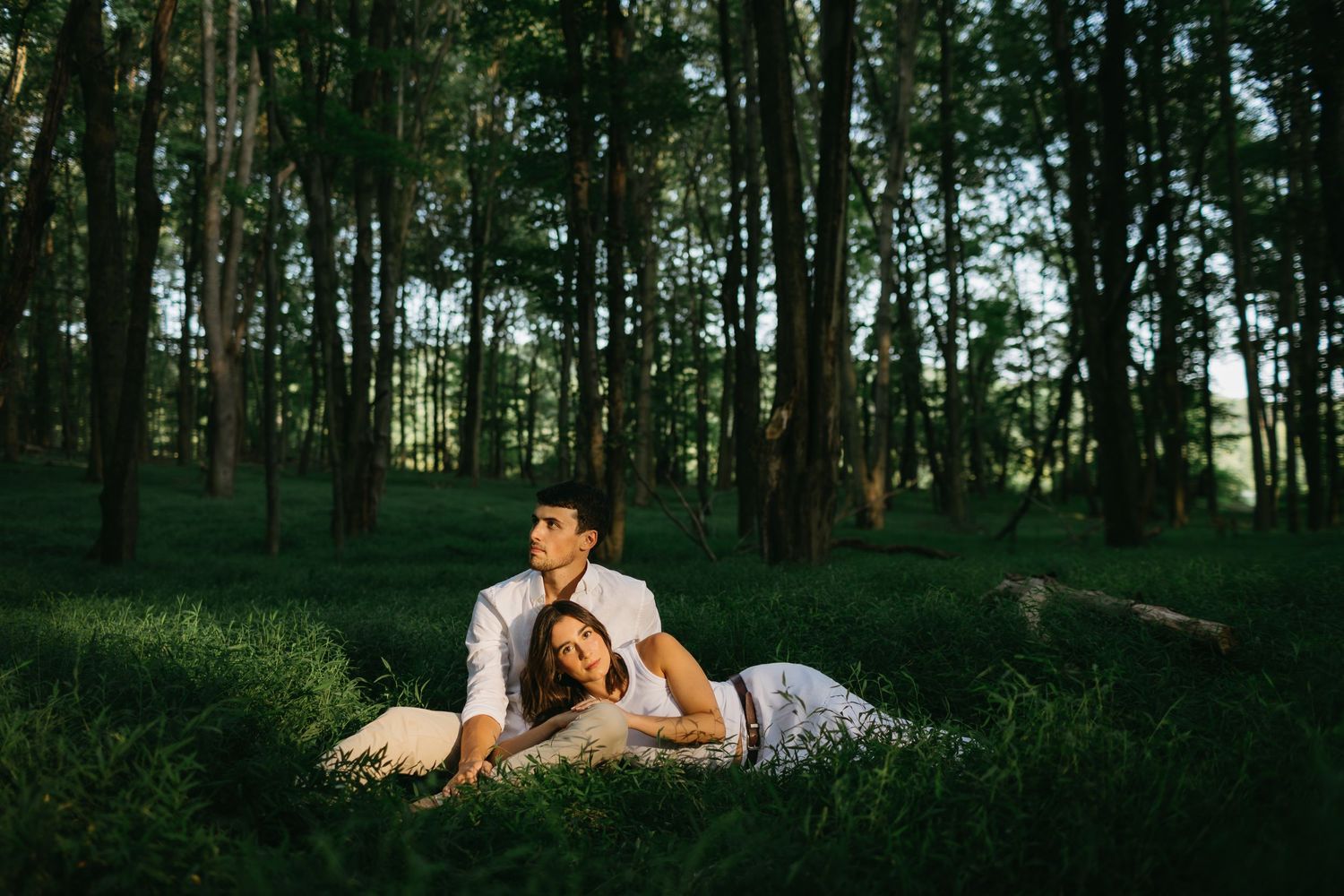 Romantic couple lying in serene forest setting during golden hour.