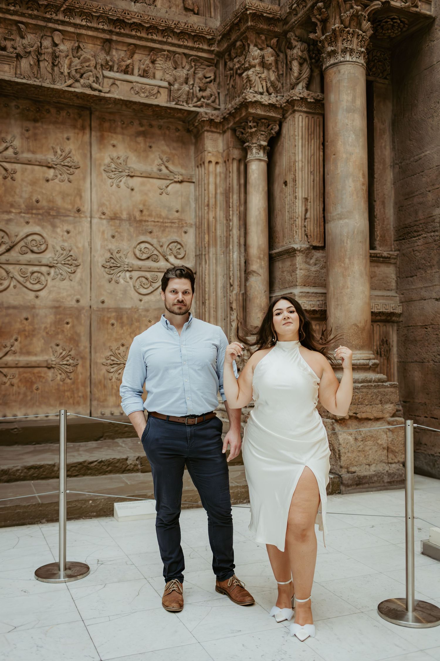 Couple posing in front of ornate stone cathedral doors and columns.