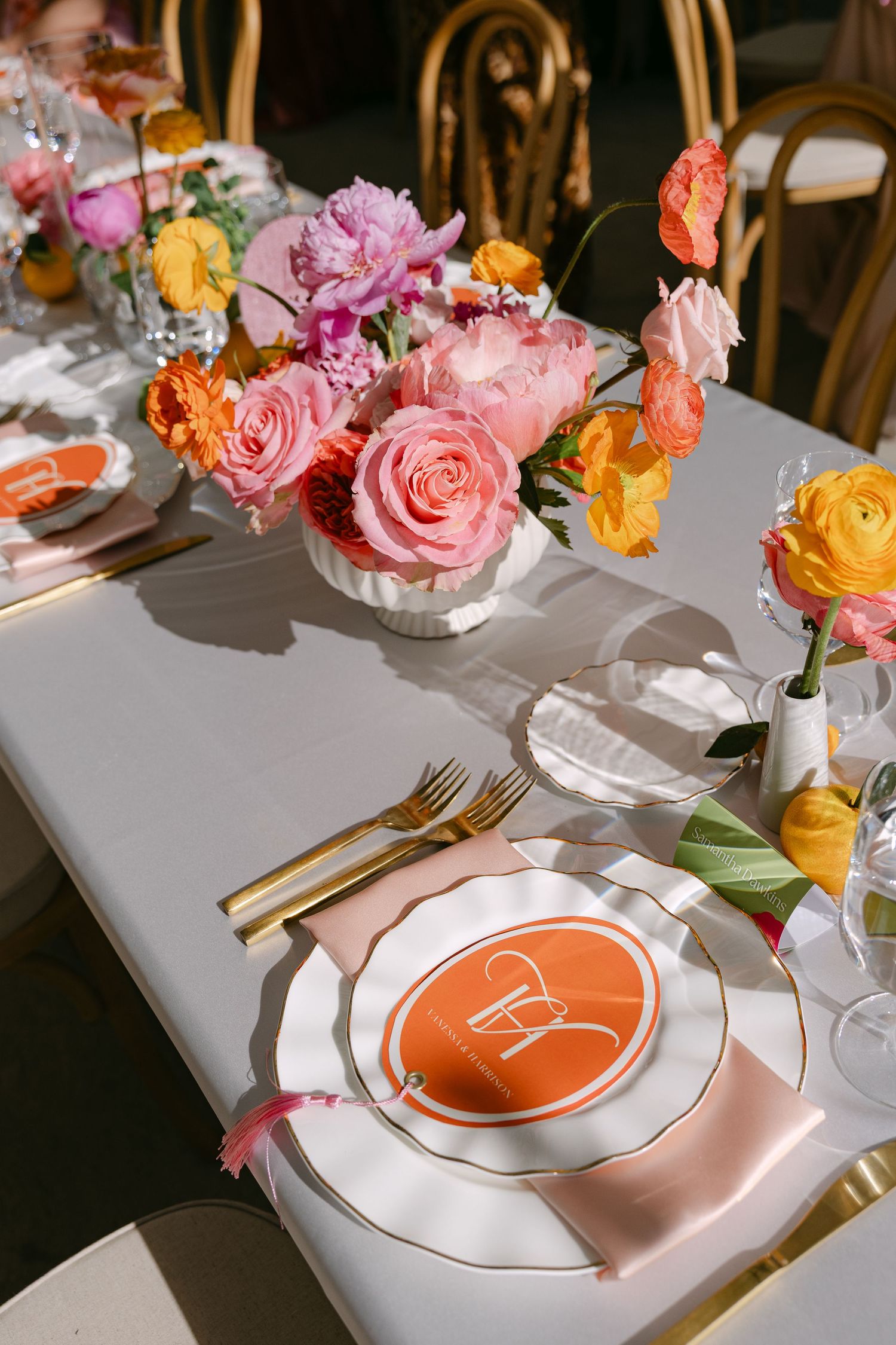 Elegant wedding tablescape with pink and orange floral centerpieces, gold cutlery, and orange monogram place cards.