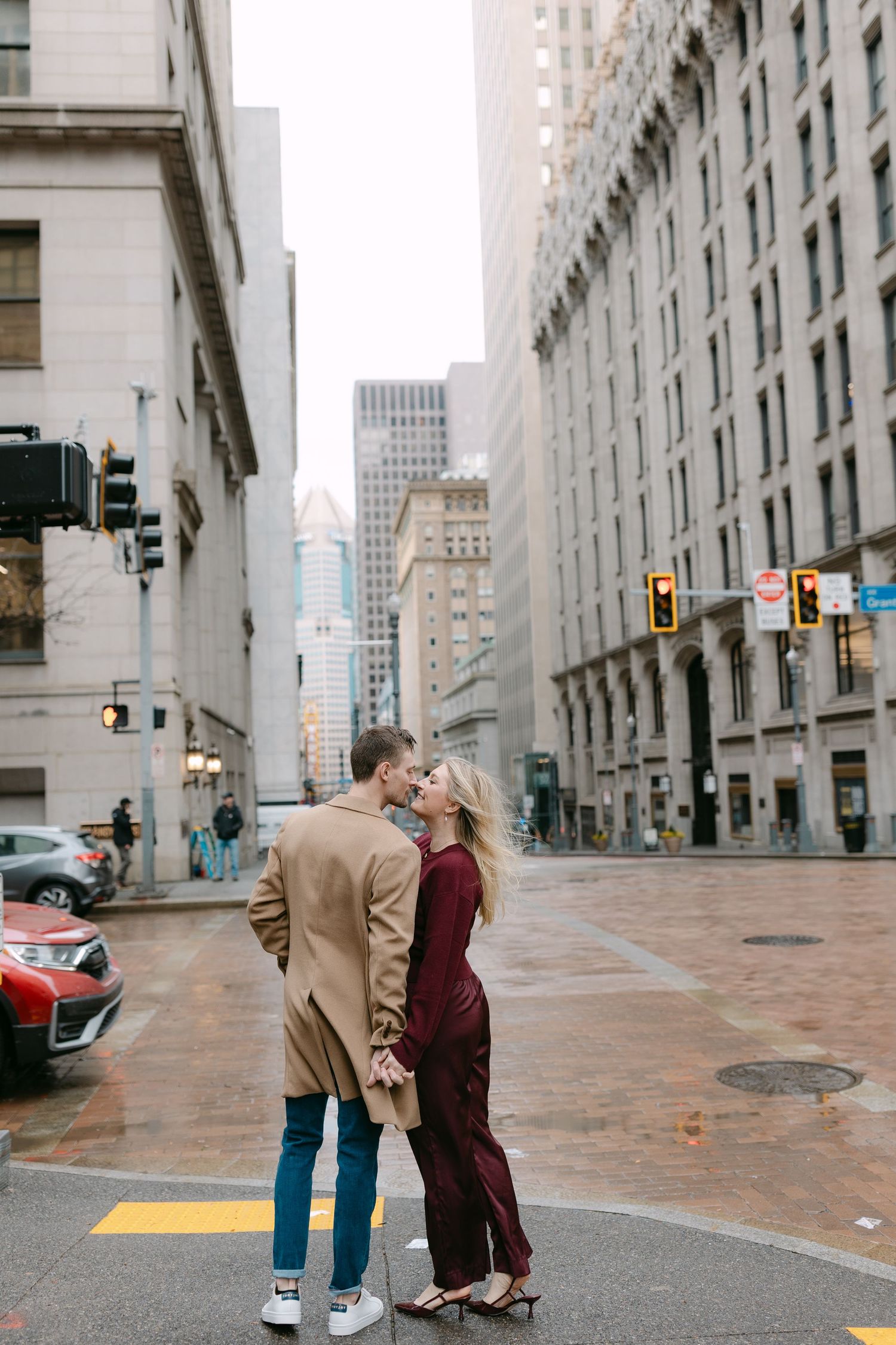 Couple sharing a romantic moment on a rainy city street corner with tall buildings and traffic lights in downtown.