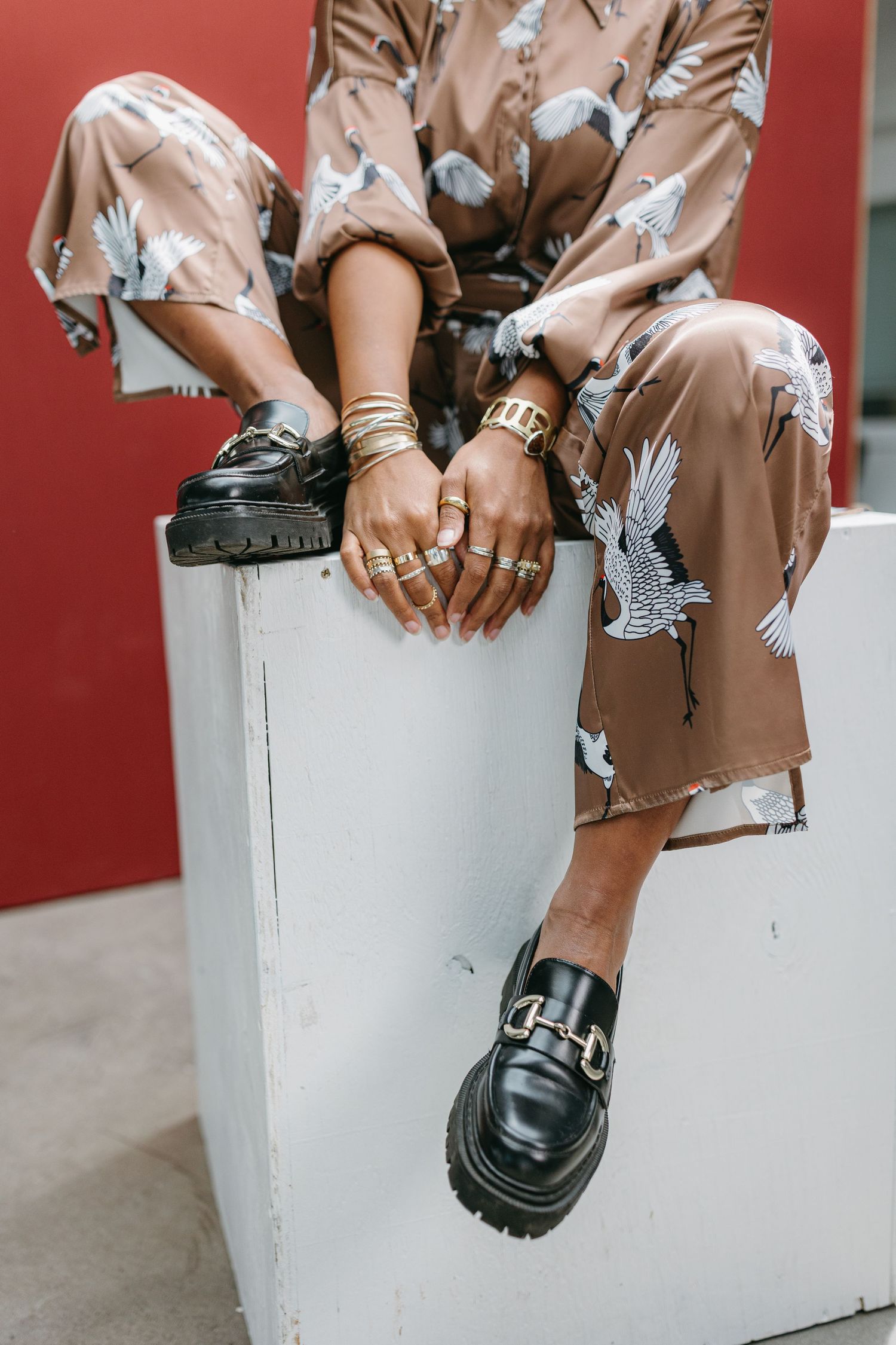 Fashion detail shot showing chunky black loafers and a brown printed dress with bird motifs against a white ledge.