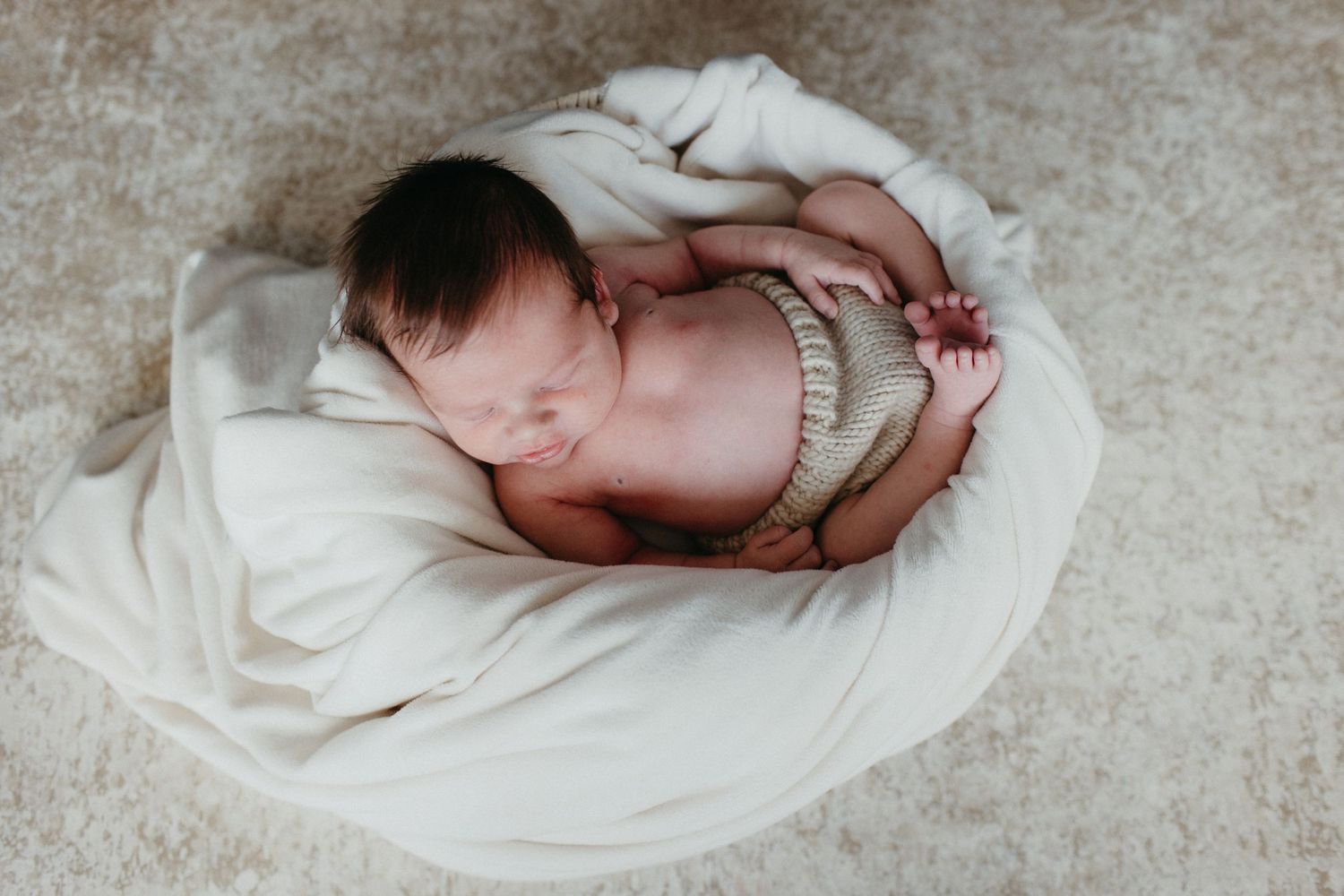A sleeping newborn baby curled up on a white blanket.