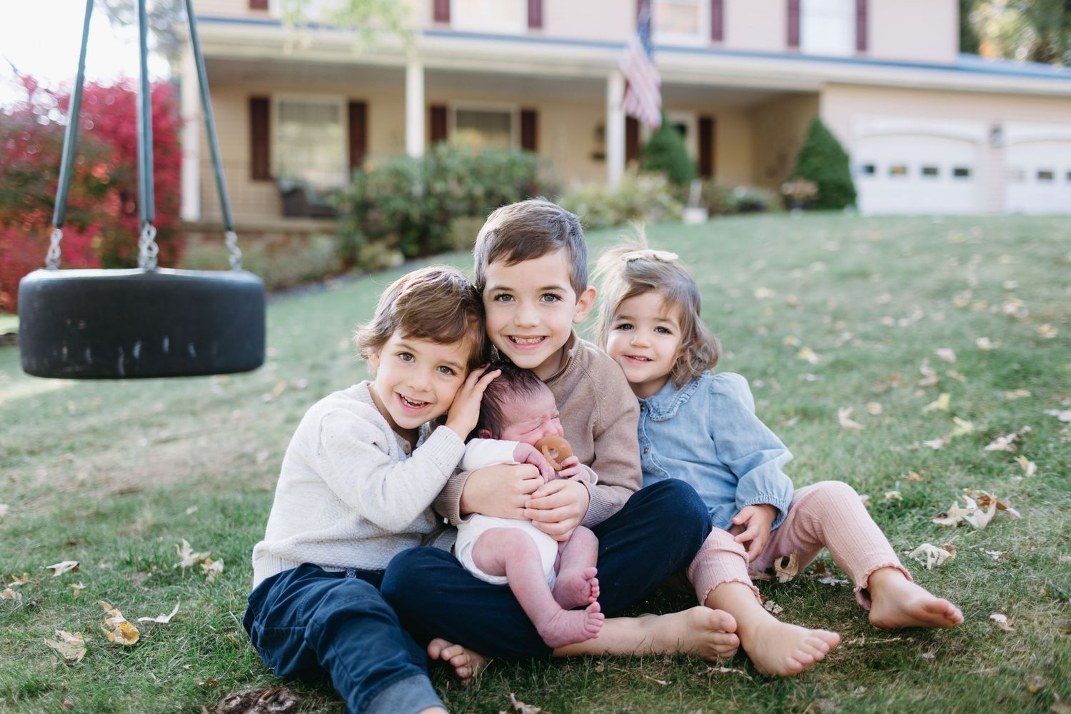 Four children sit together on grass near a tire swing.