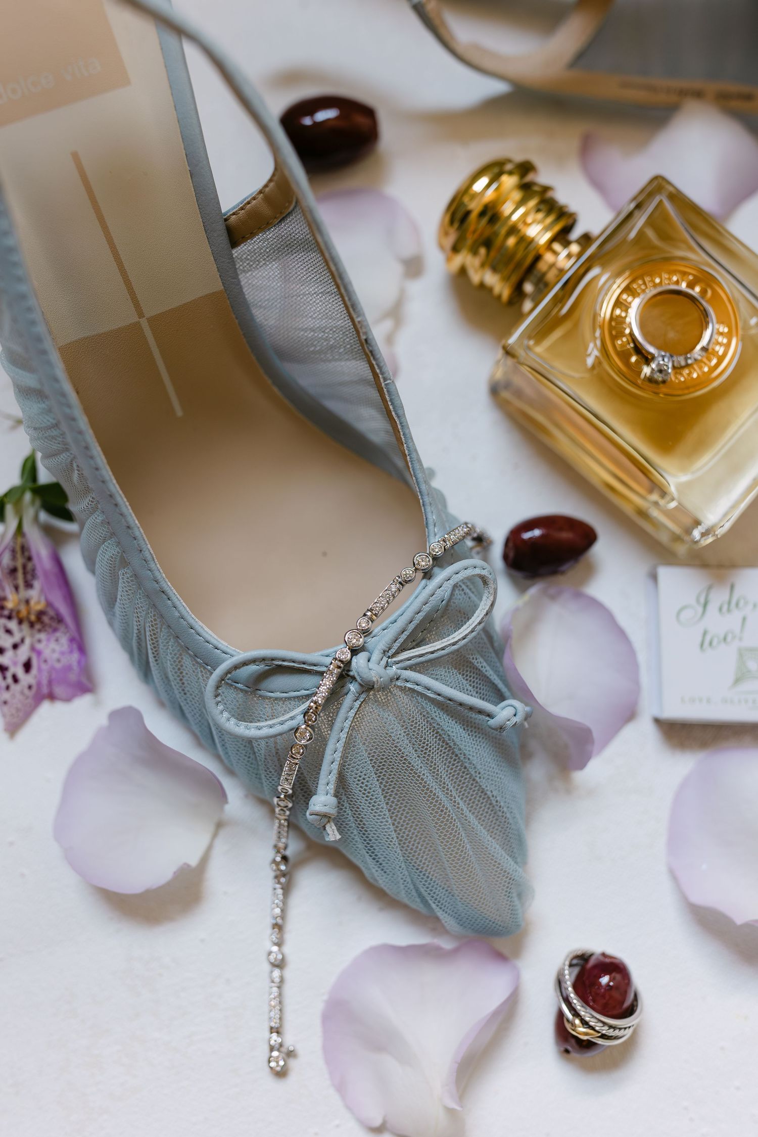 Elegant pale blue ballet flat with crystal bow detail displayed with perfume bottle and rose petals.