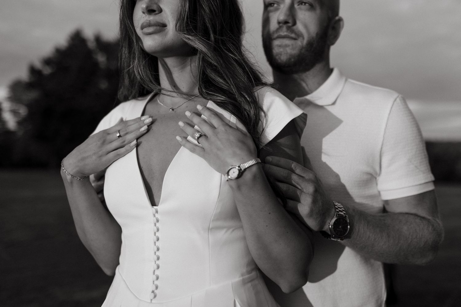 Romantic black and white portrait of a couple embracing in a simple white dress and casual attire at sunset.