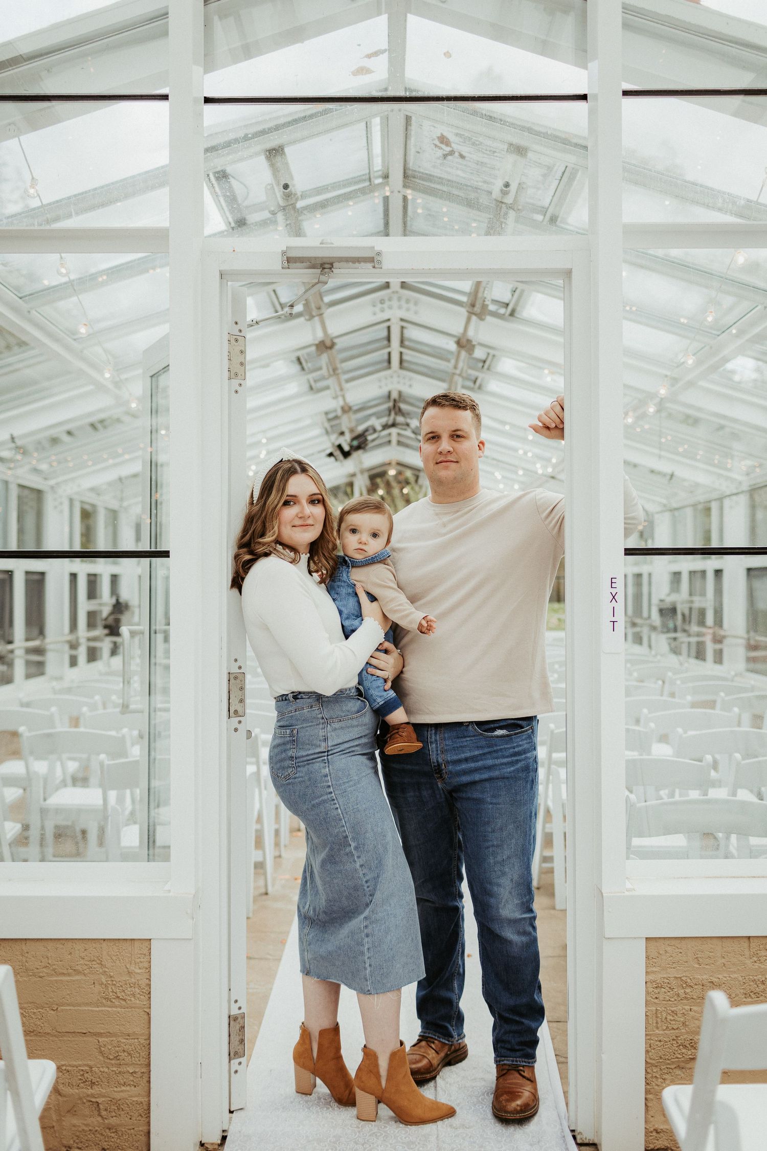 Family posing together in a bright greenhouse with natural light streaming through glass panels.