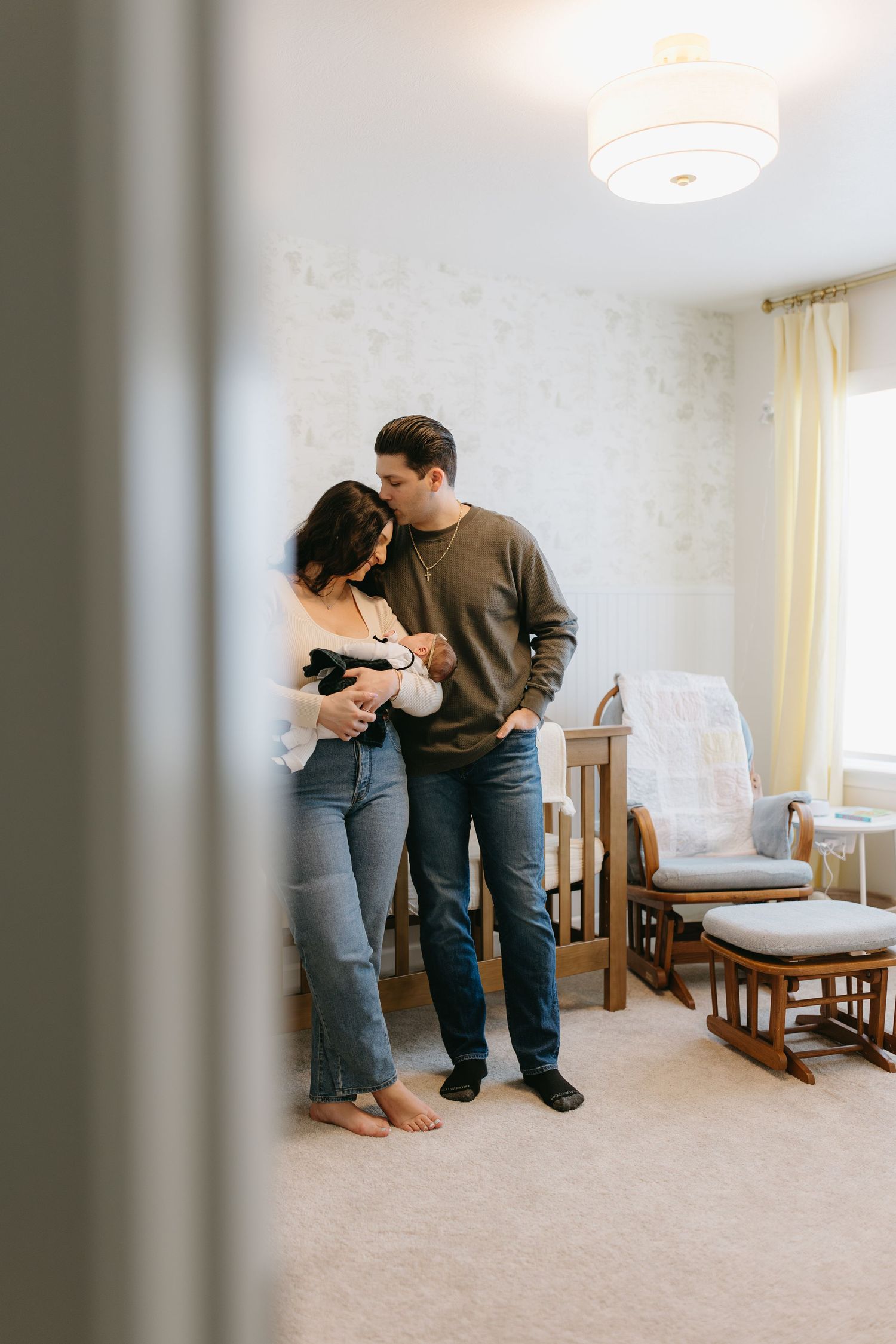 An intimate nursery scene showing parents cradling their newborn by a window.
