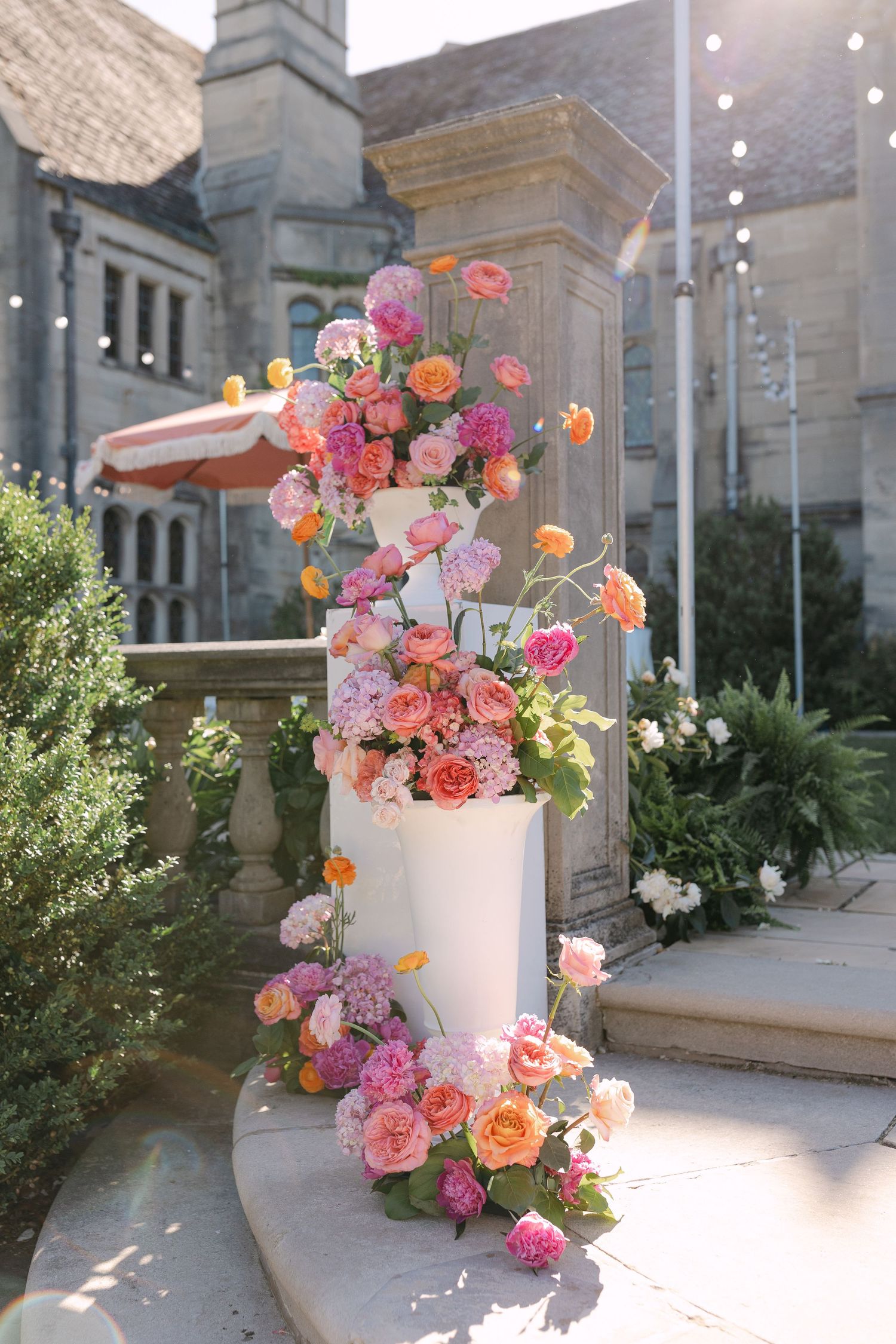 Elegant three-tier white wedding cake adorned with colorful pink, peach, and orange floral arrangements outdoors.