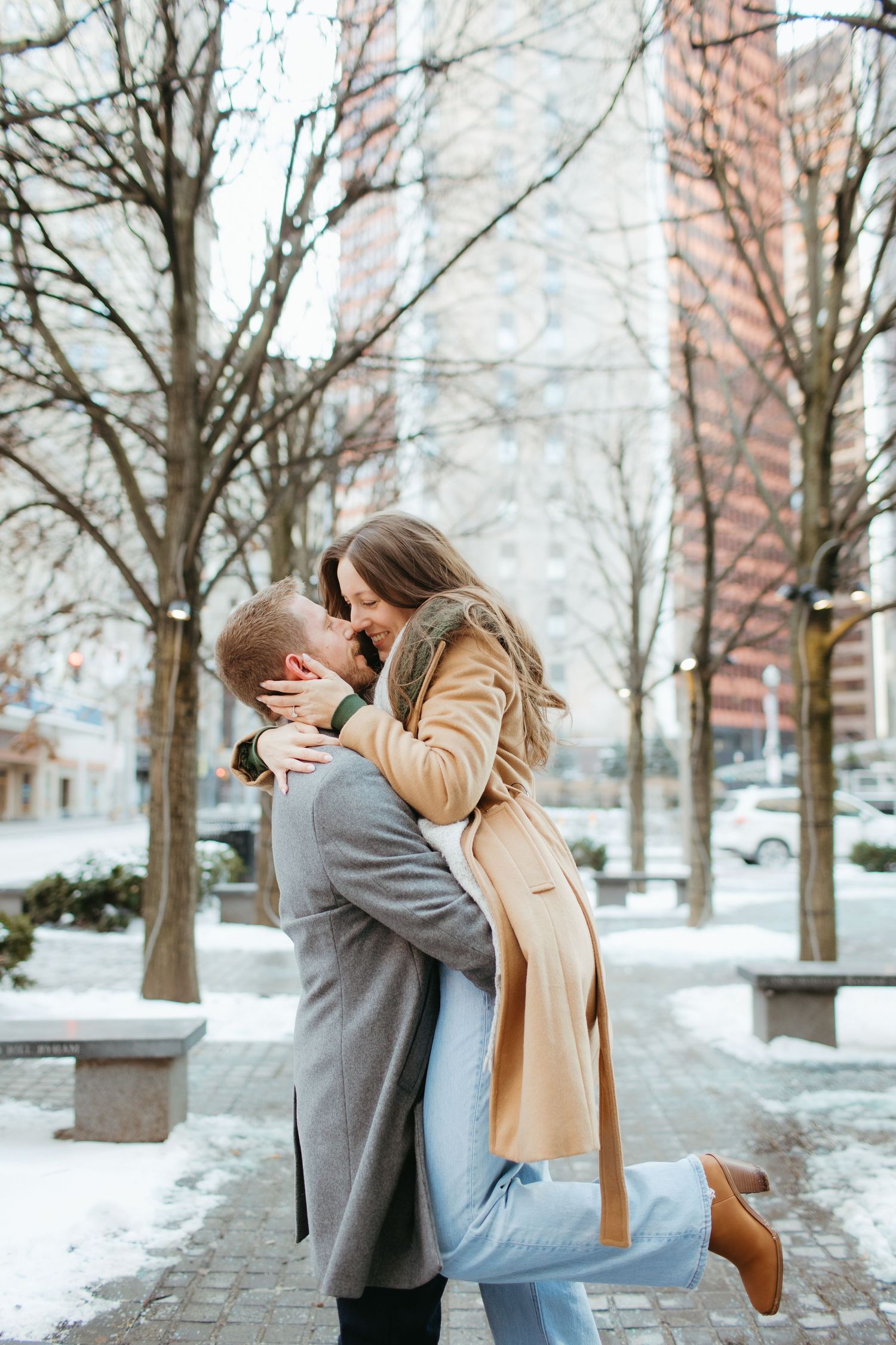 A romantic winter scene with a couple embracing on a snowy urban sidewalk.