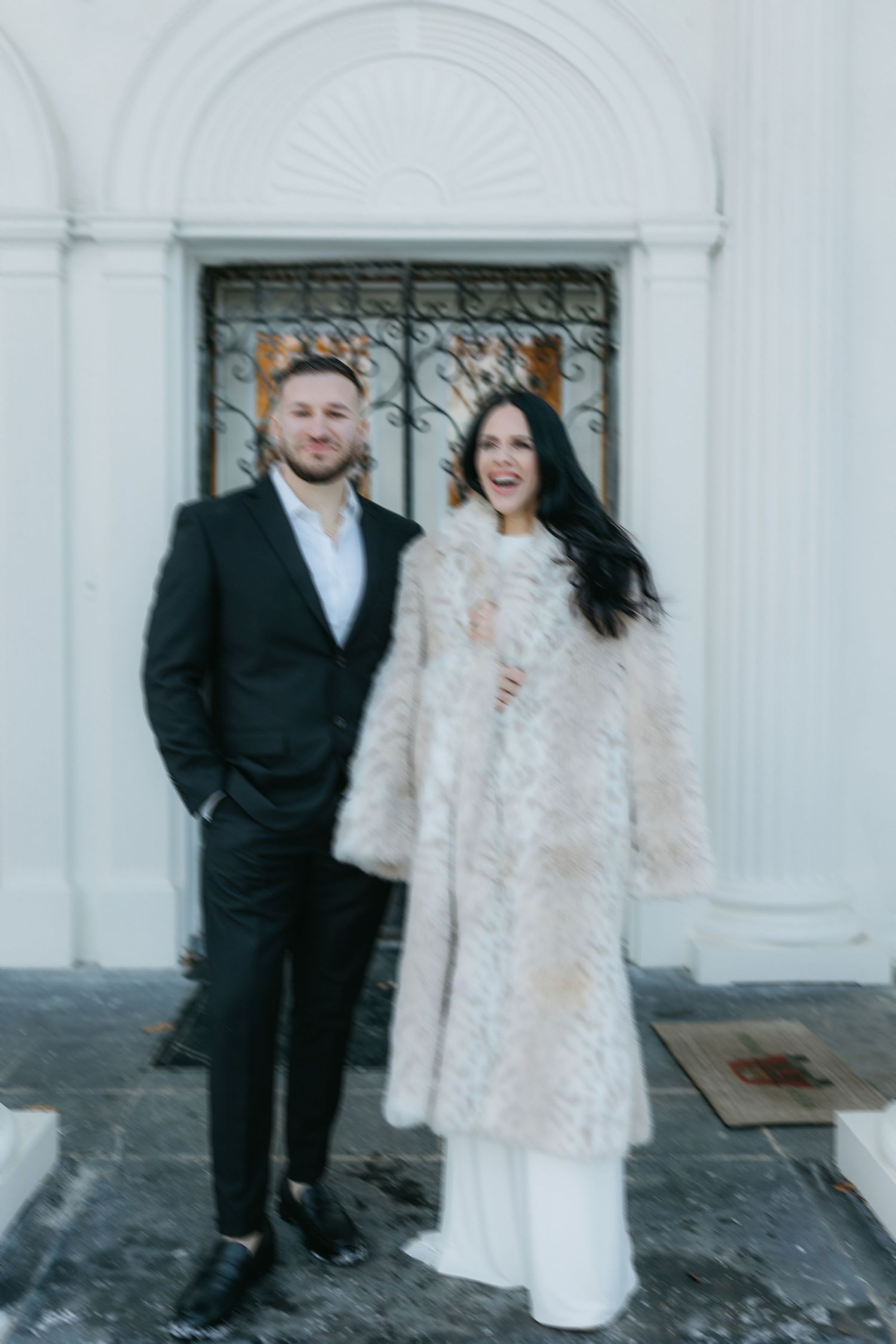 Couple in winter wedding attire standing in front of white columned entrance.