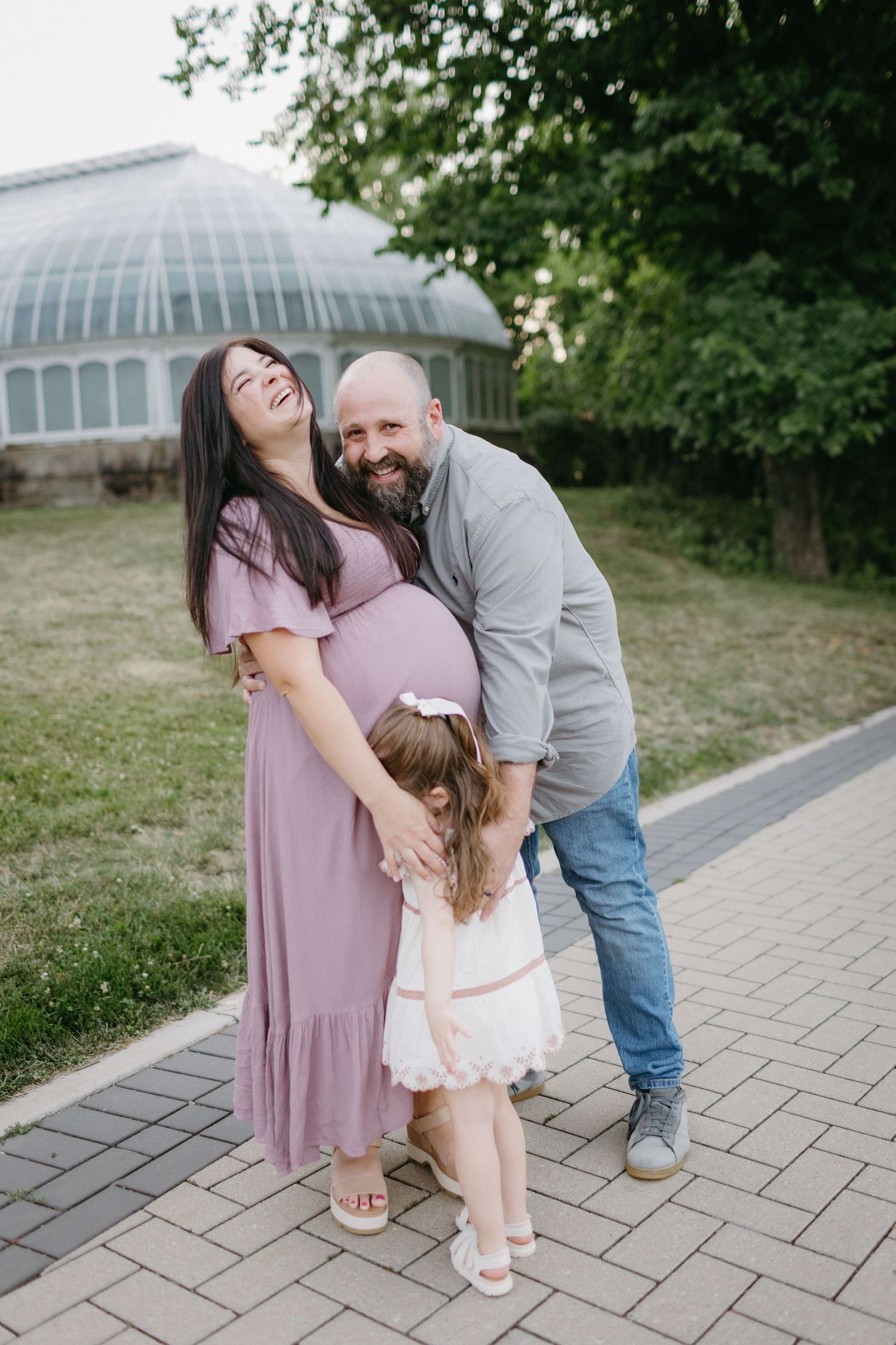 A playful family moment captured outside a glass conservatory building on a paved pathway.
