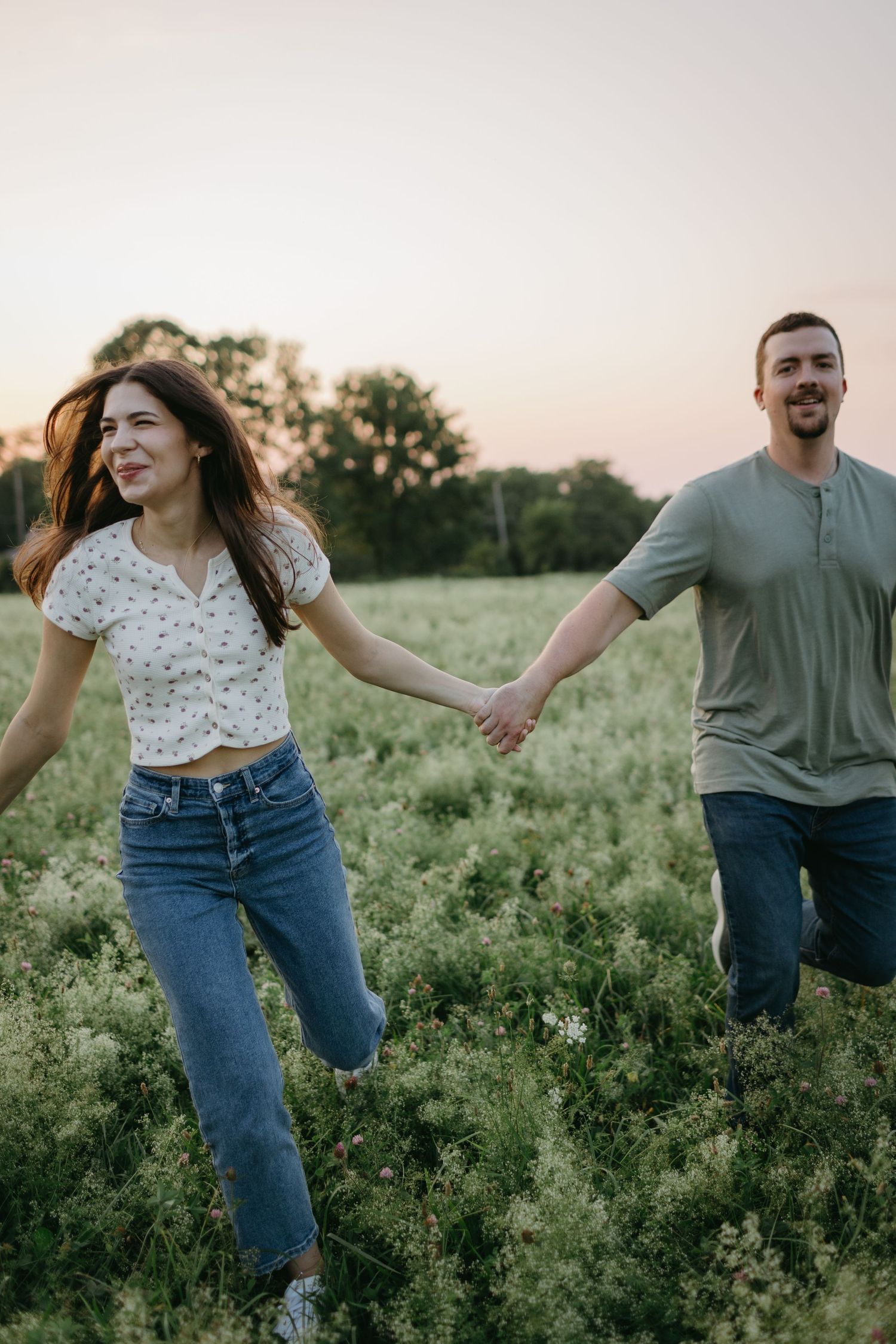 Playful couple running through wildflower field at sunset.