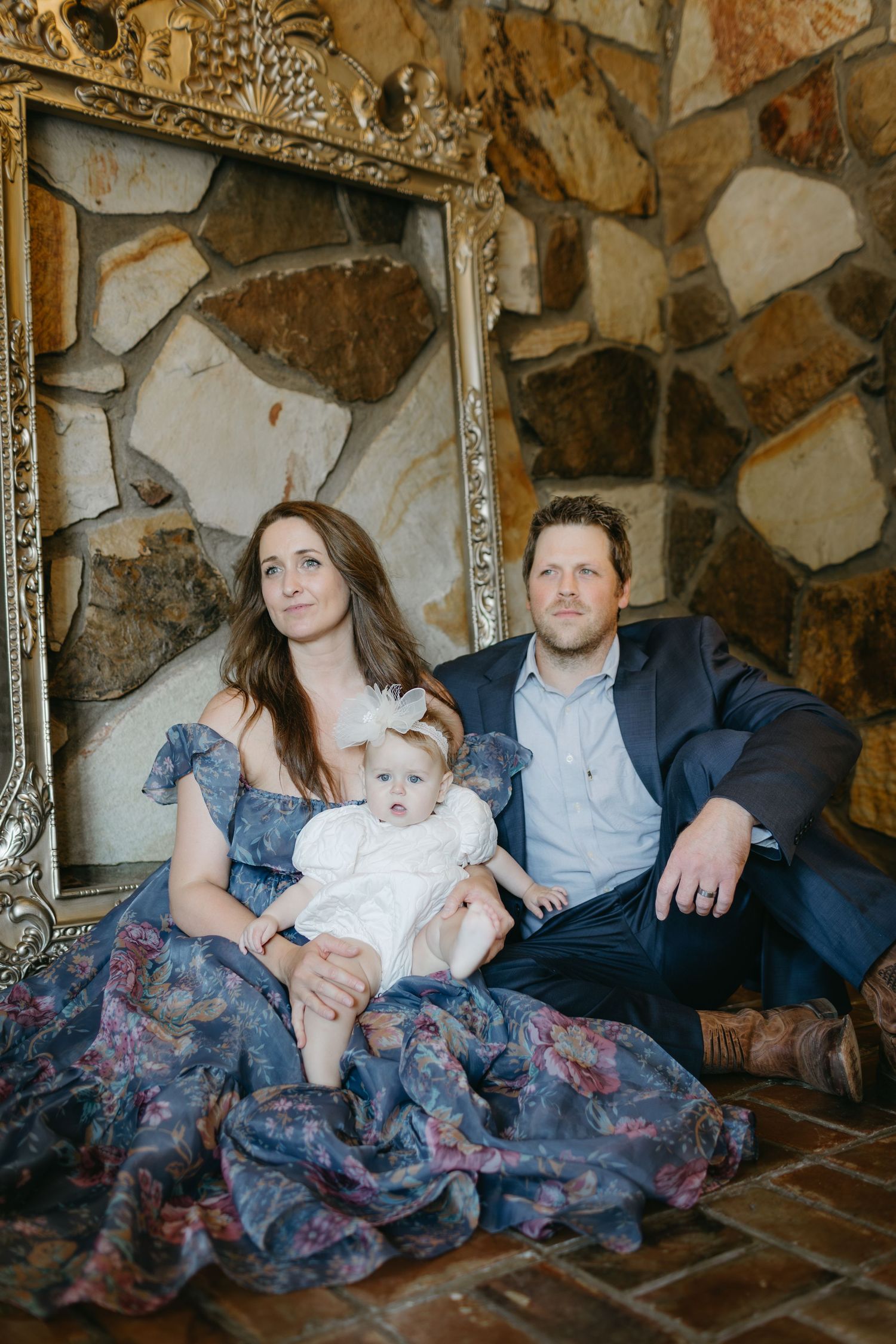 Family portrait in front of stone wall with ornate vintage frame and flowing blue floral dress.