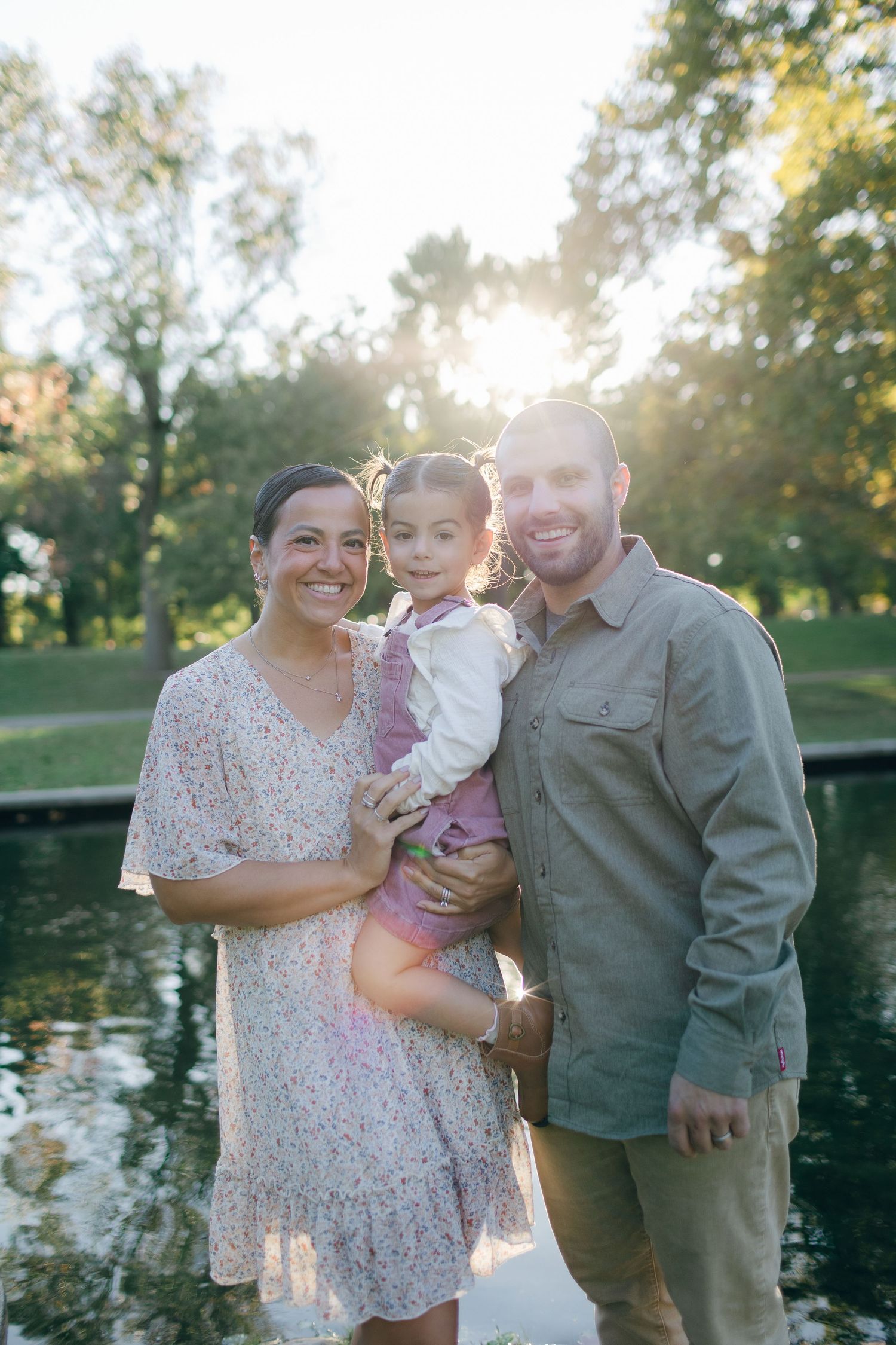 Family poses together by a pond at sunset in a park setting.