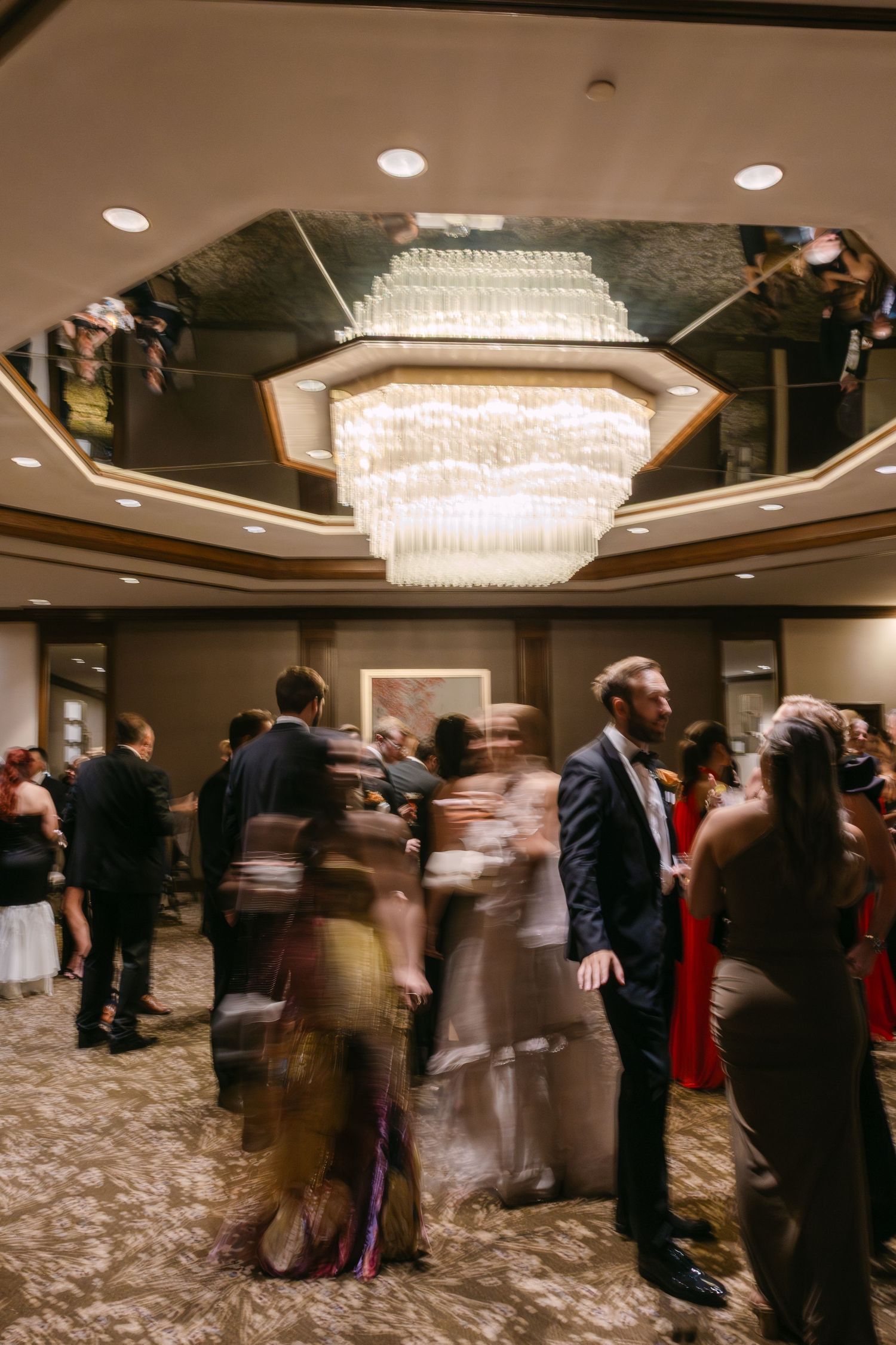 Motion blur captures dancers spinning across an elegant ballroom floor beneath crystal chandeliers at an evening event.