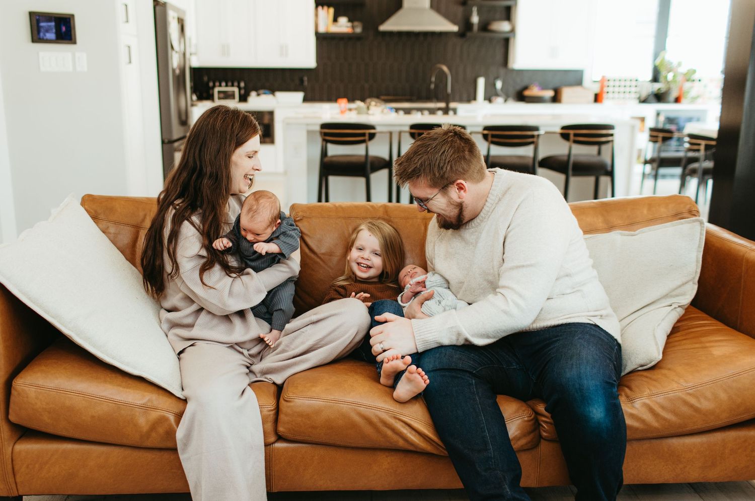A family shares a tender moment together on a brown leather couch in their living room.