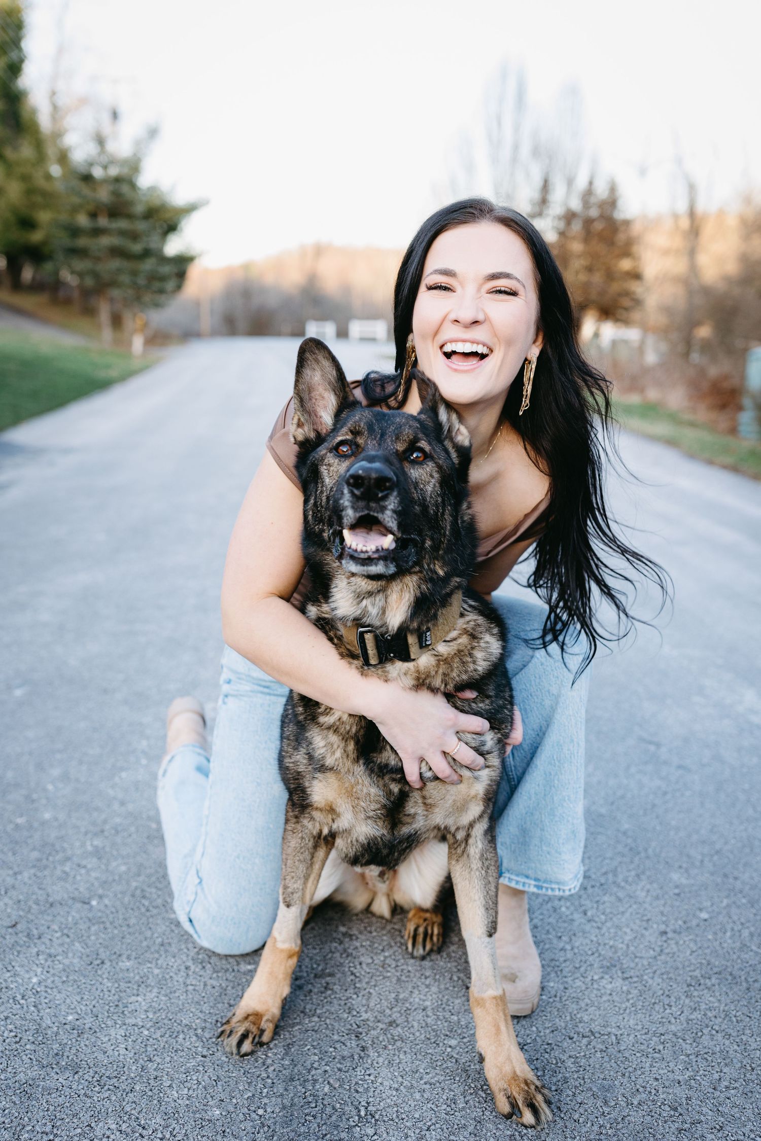 Woman hugging and smiling with her German Shepherd dog on a paved pathway.