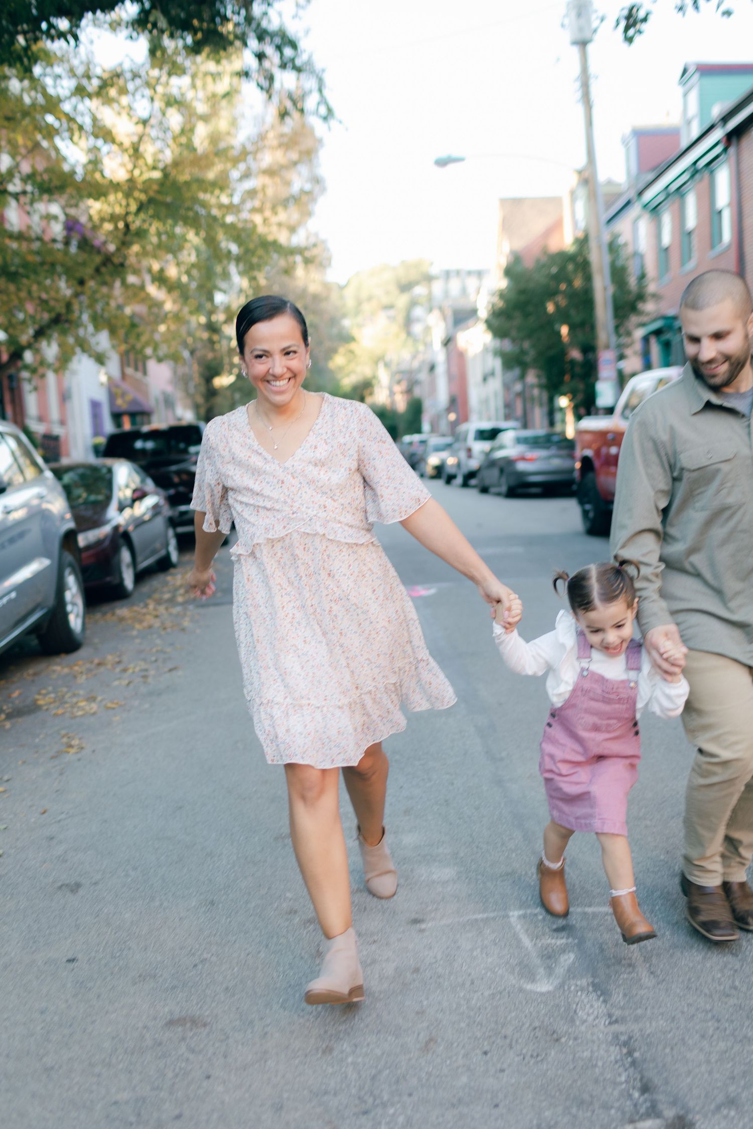 Family walking together on urban street lined with parked cars during golden hour.