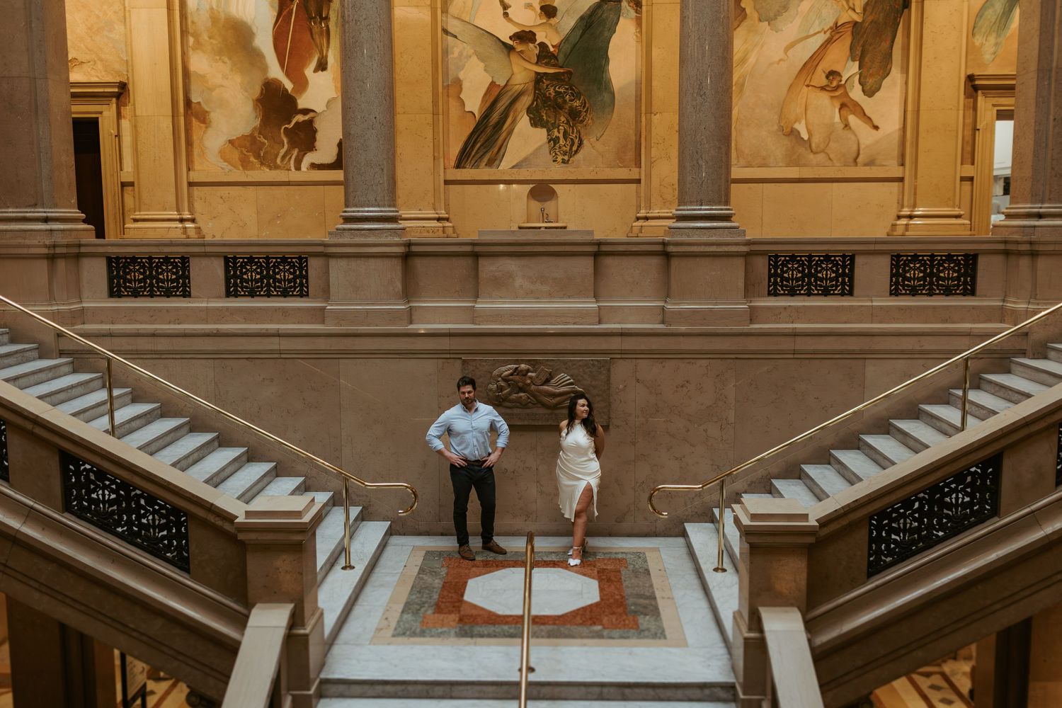 Elegant interior shot of couple standing at grand staircase landing in museum.