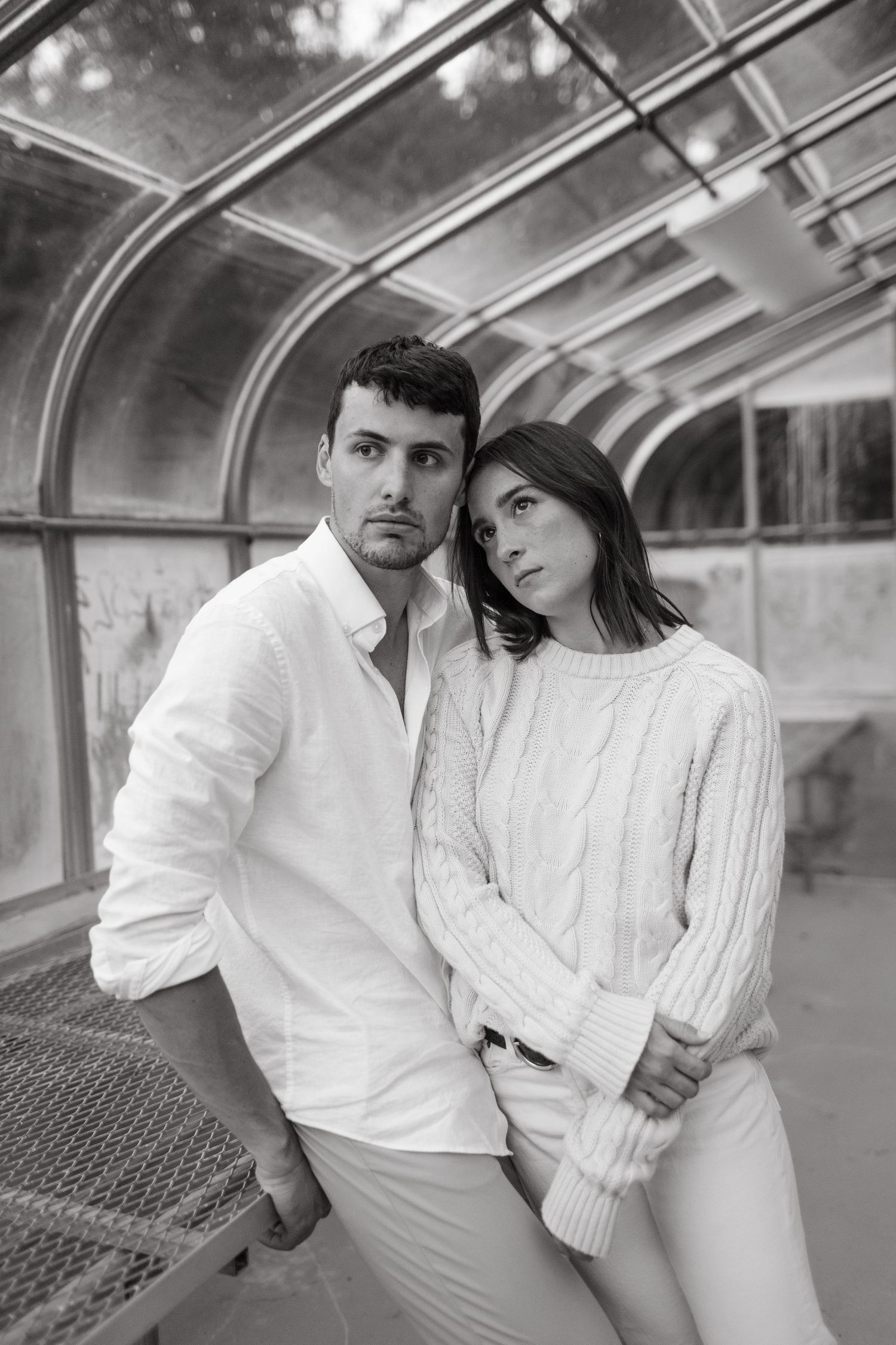 Stylish couple in white poses in greenhouse with curved glass ceiling.