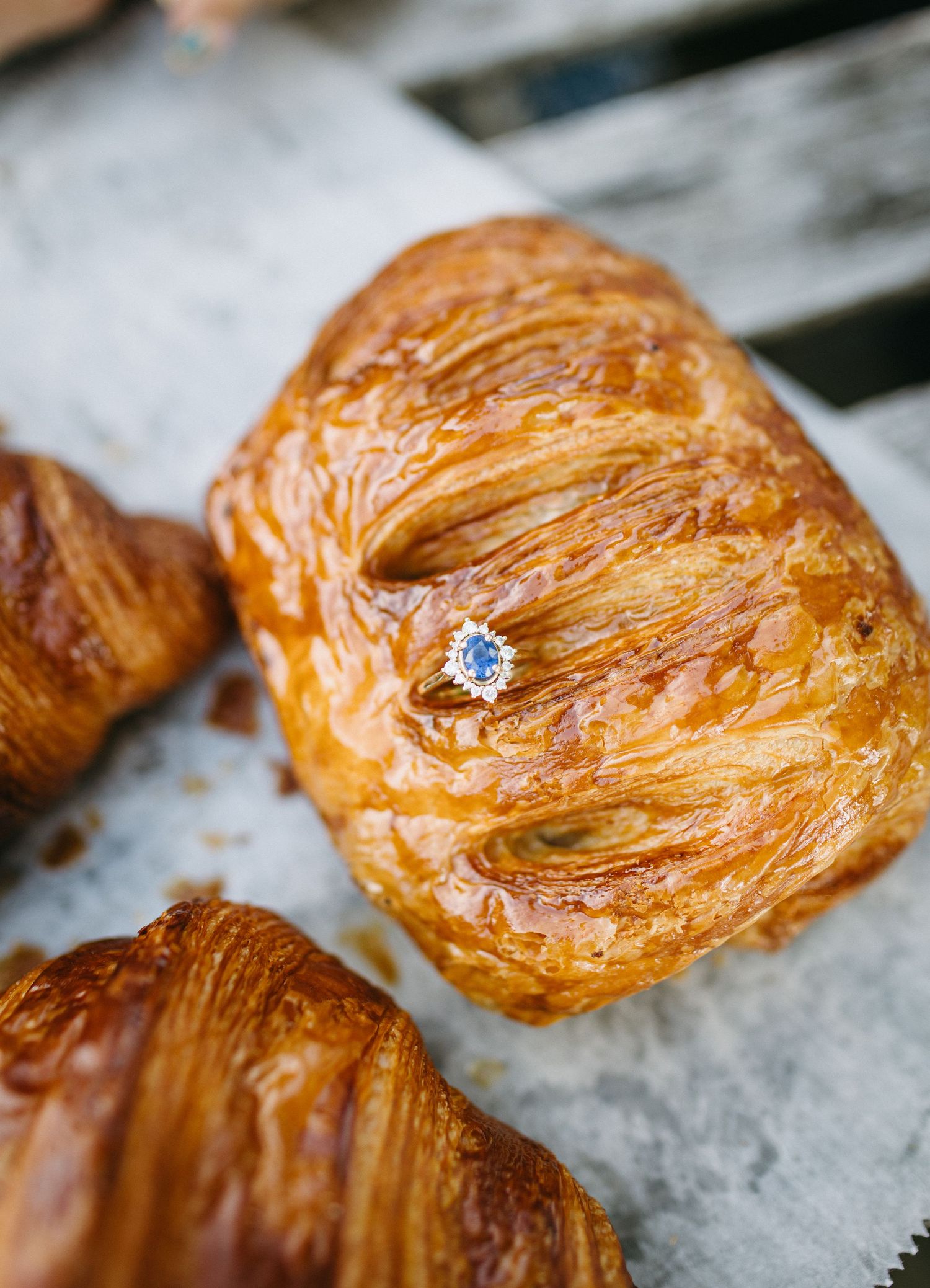 Diamond engagement ring placed on a golden flaky croissant pastry.