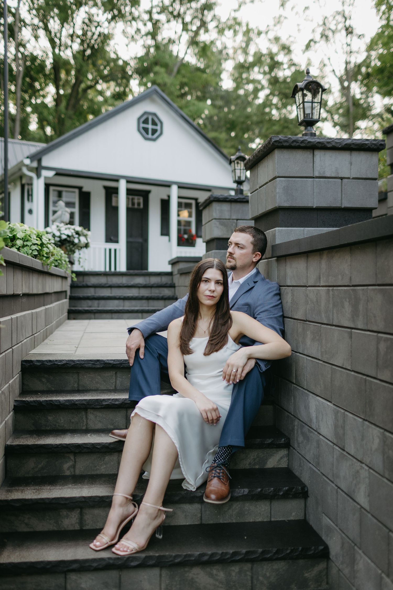Couple sitting together on concrete steps with white house in background.