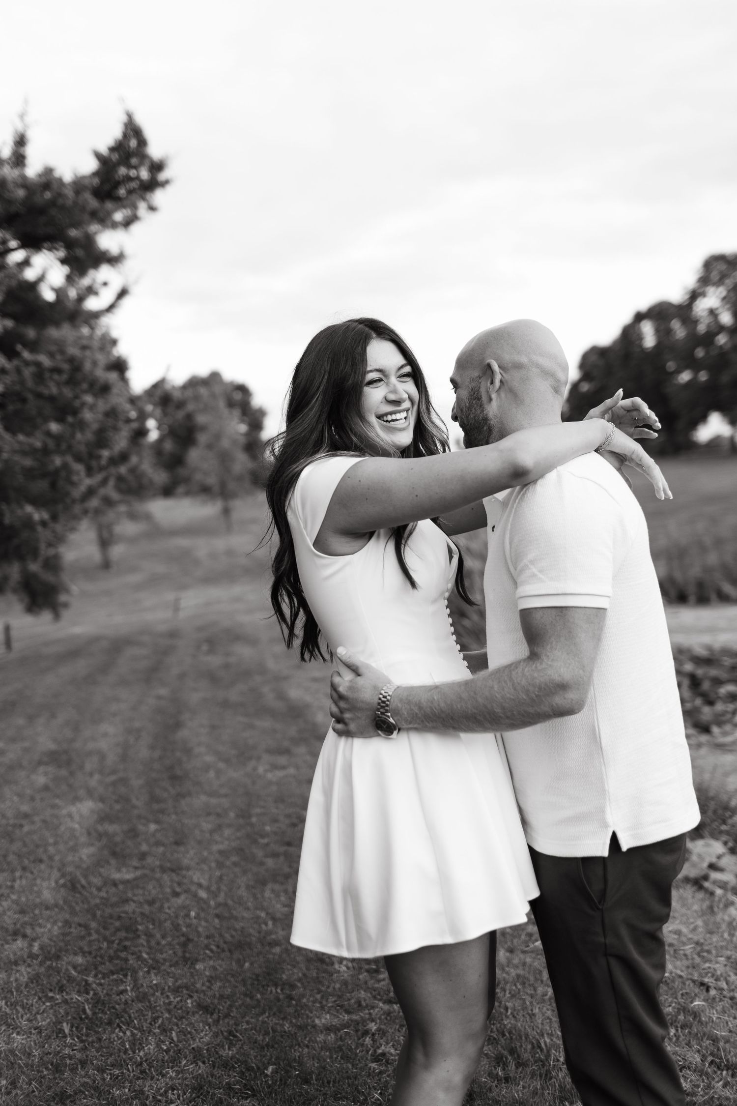 Black and white photo of joyful couple embracing on golf course path.