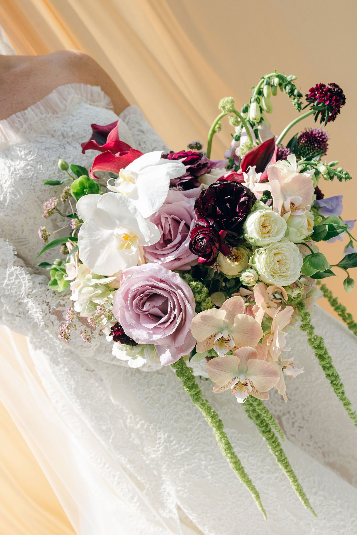 A delicate floral arrangement featuring pink roses, white flowers and deep purple blooms against white lace fabric.