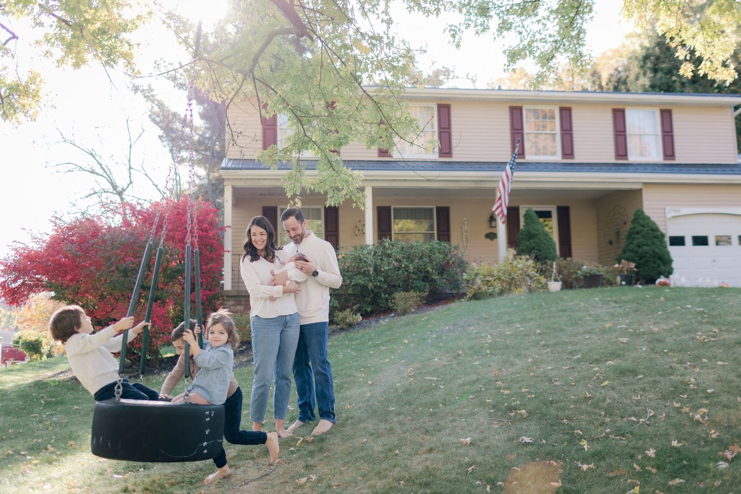 Family gathered by a tire swing outside their suburban home in autumn.