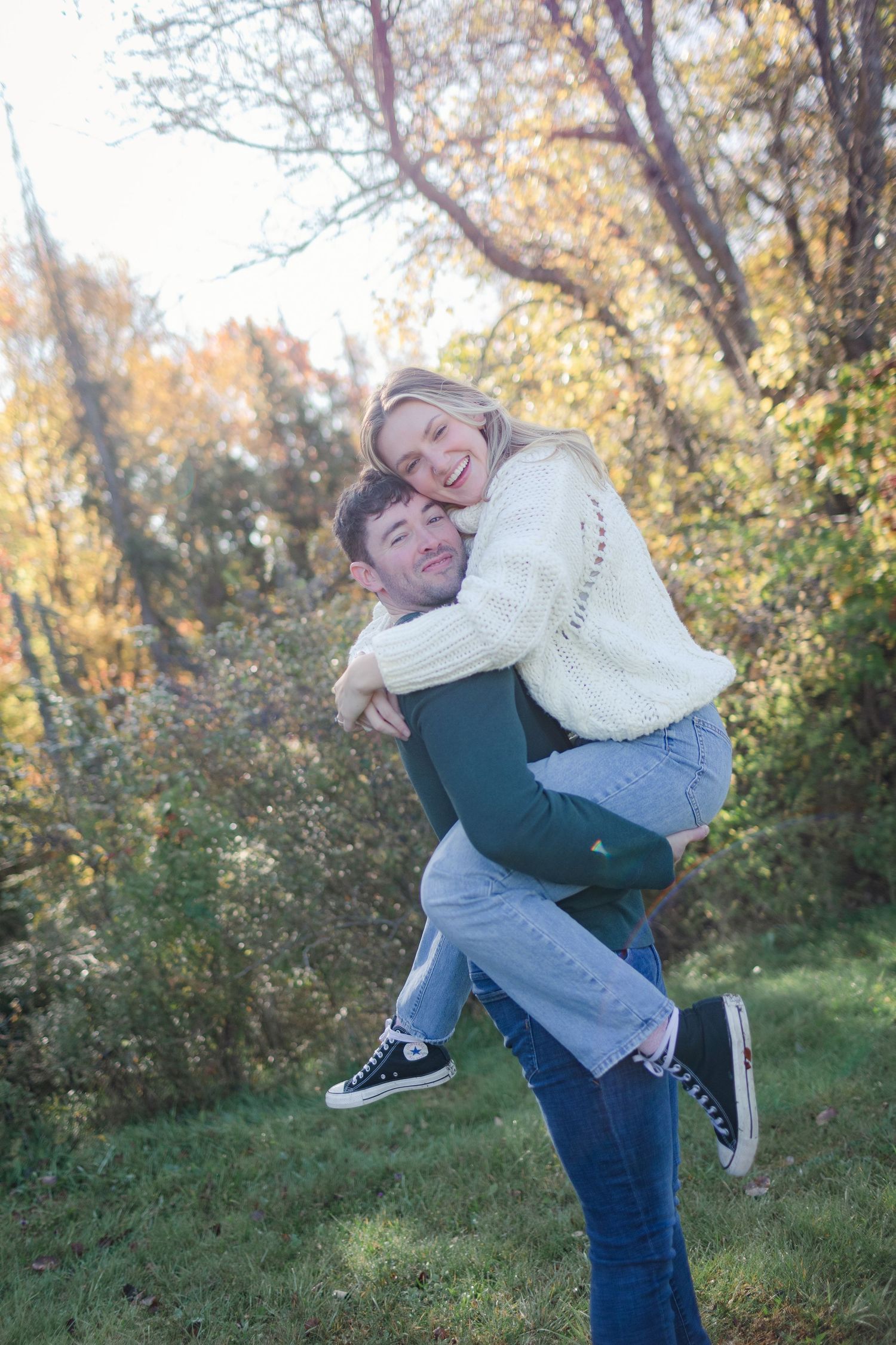 A playful couple embraces while enjoying a fall day in a park setting with golden leaves.