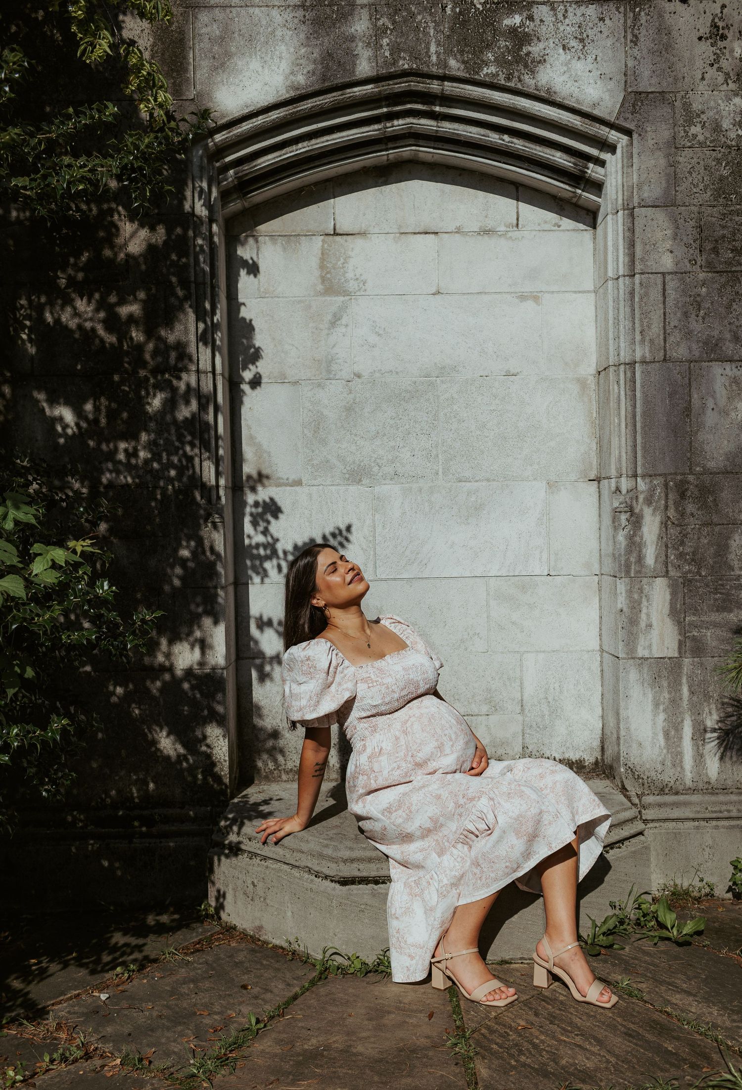 A person in a white dress poses against a stone archway in dramatic lighting.