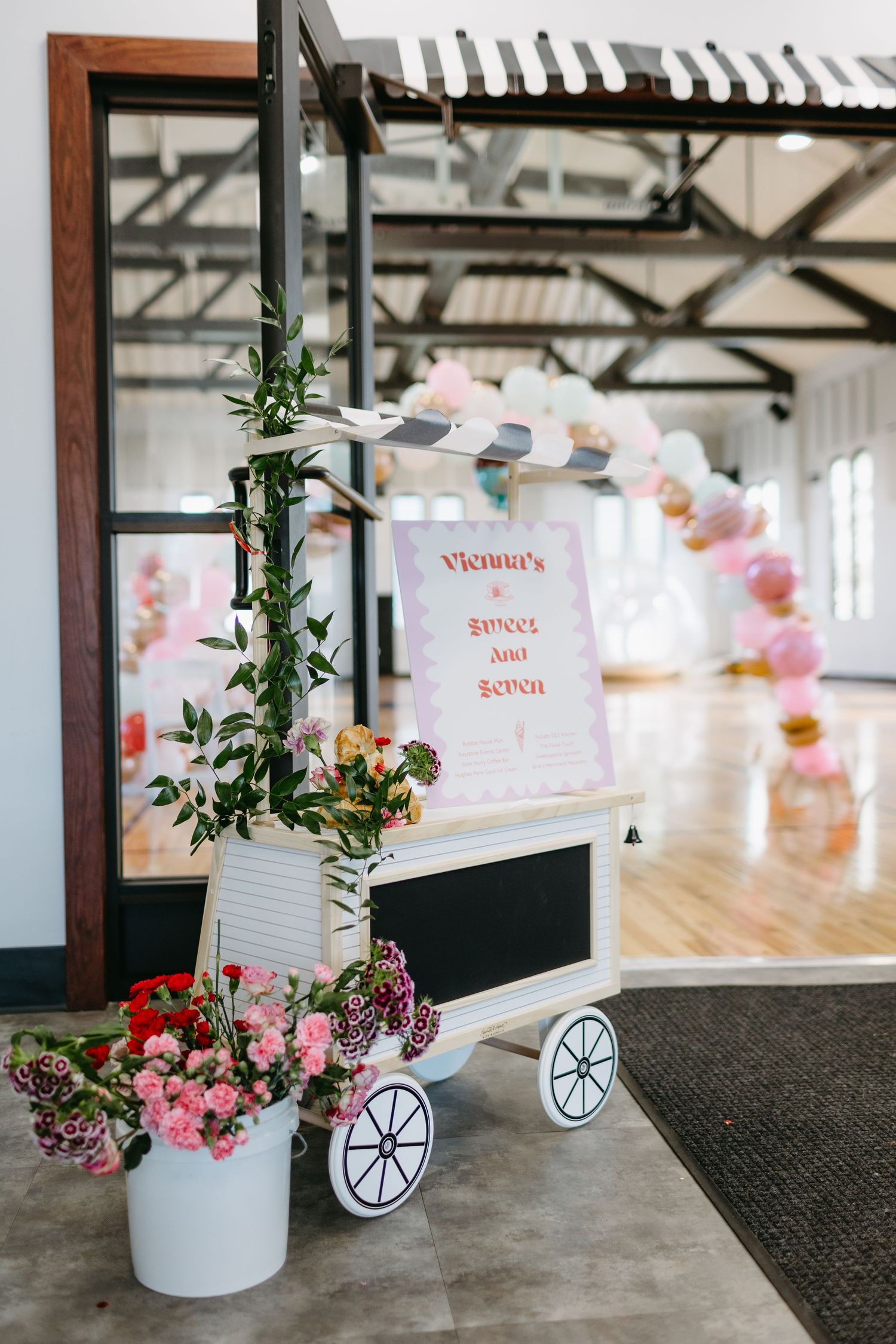 A decorative flower cart display with pink blooms and signage at an event venue.