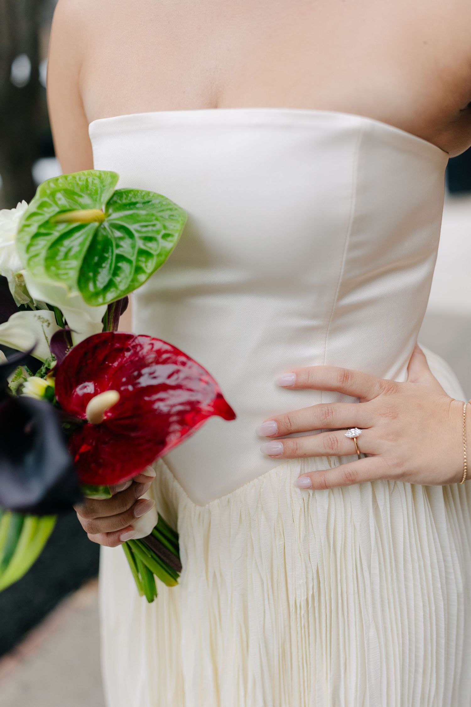 Close-up view of a white wedding dress with pleated texture and red floral bouquet details.