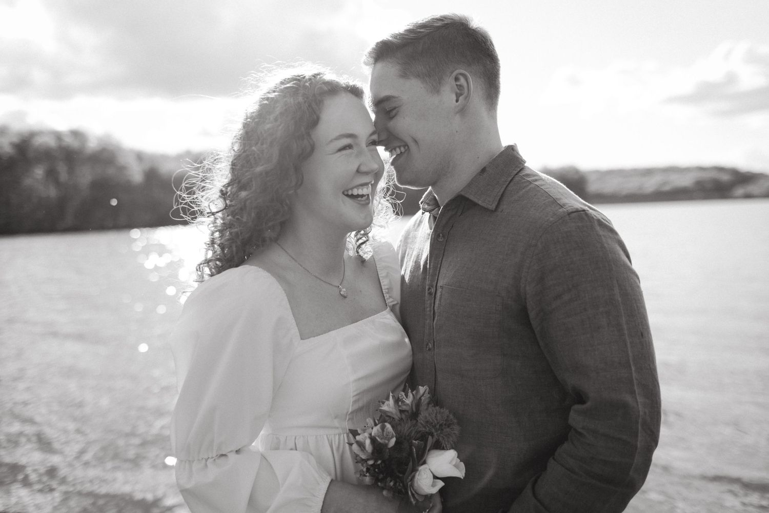 Black and white portrait of couple sharing intimate moment by waterfront.