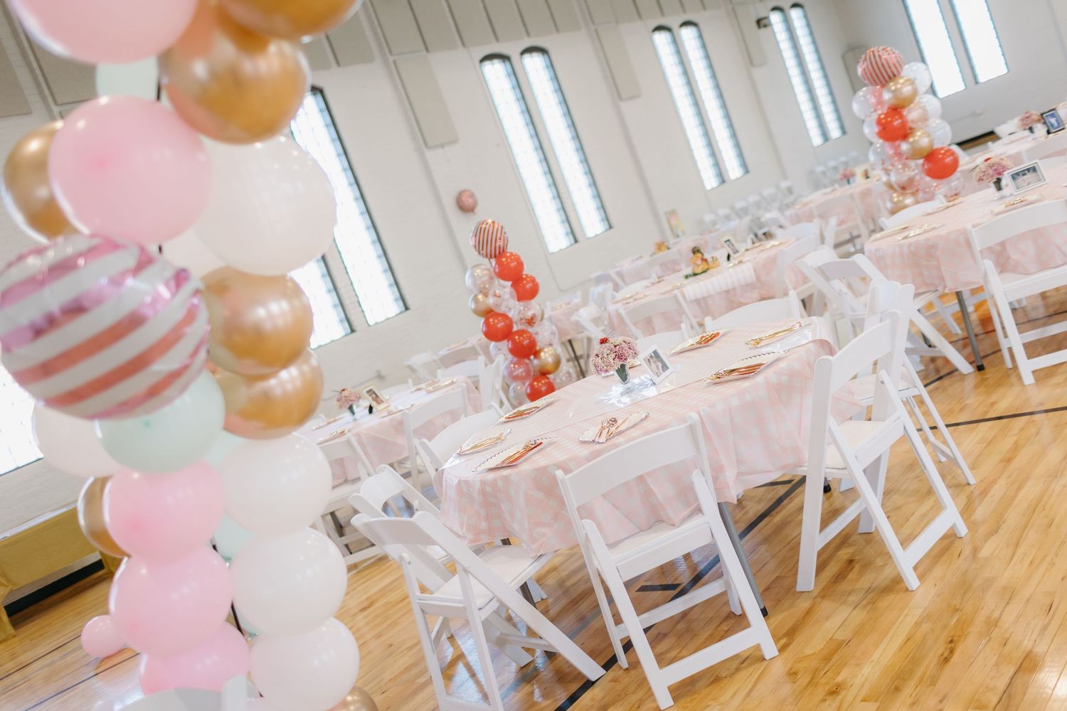 An elegant party setup with pink and gold balloons decorating white tables and chairs.
