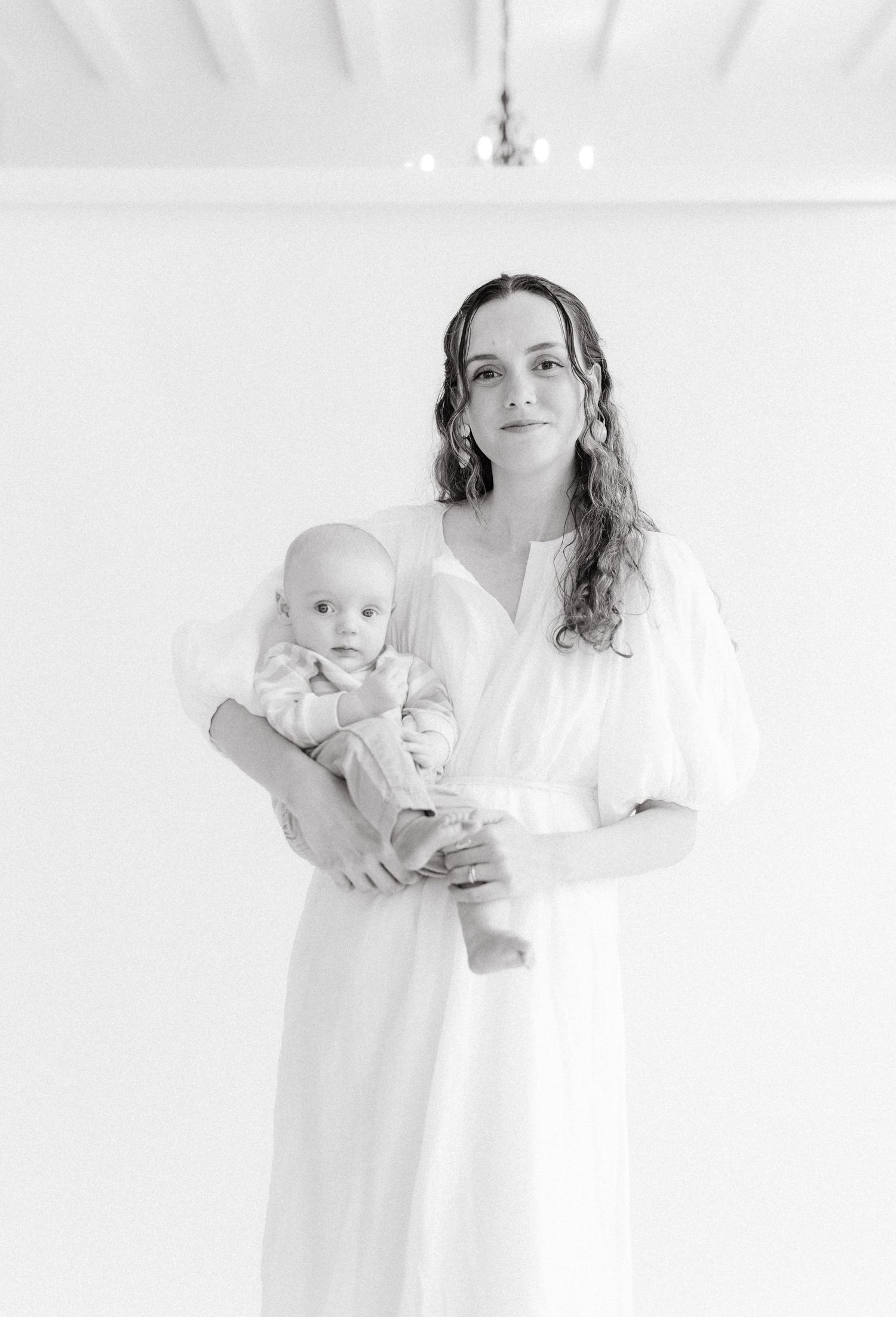Black and white portrait of woman holding infant in bright minimalist setting.