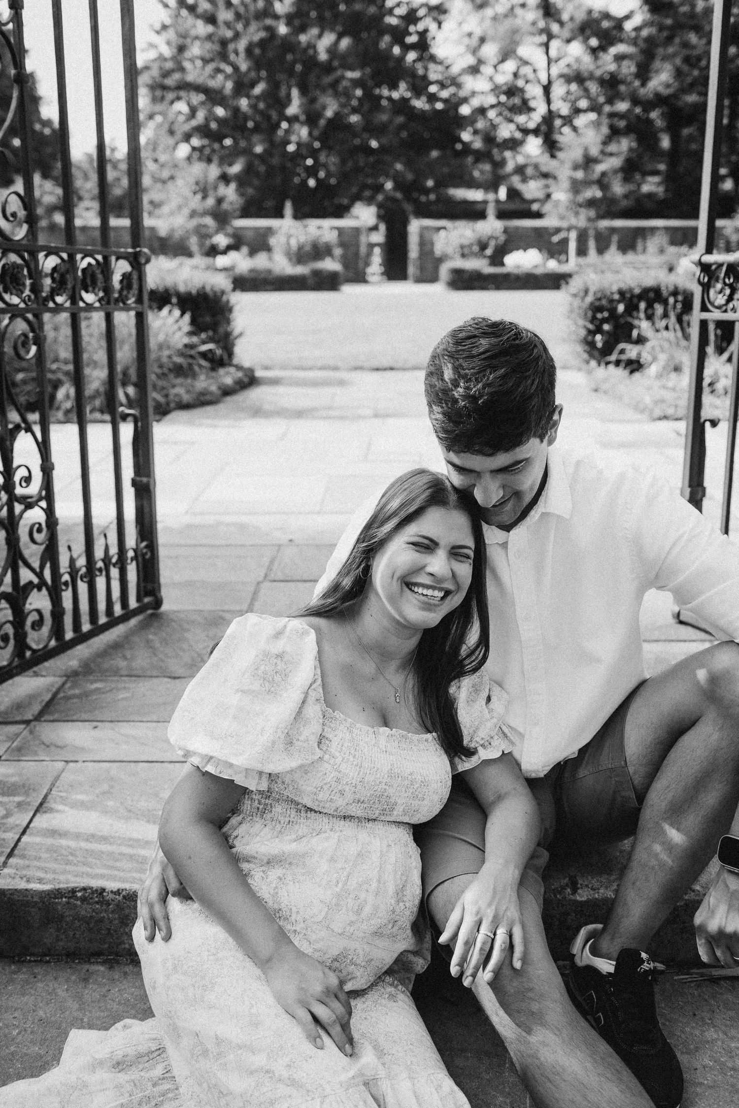 A joyful couple sits together by an ornate iron gate outdoors.