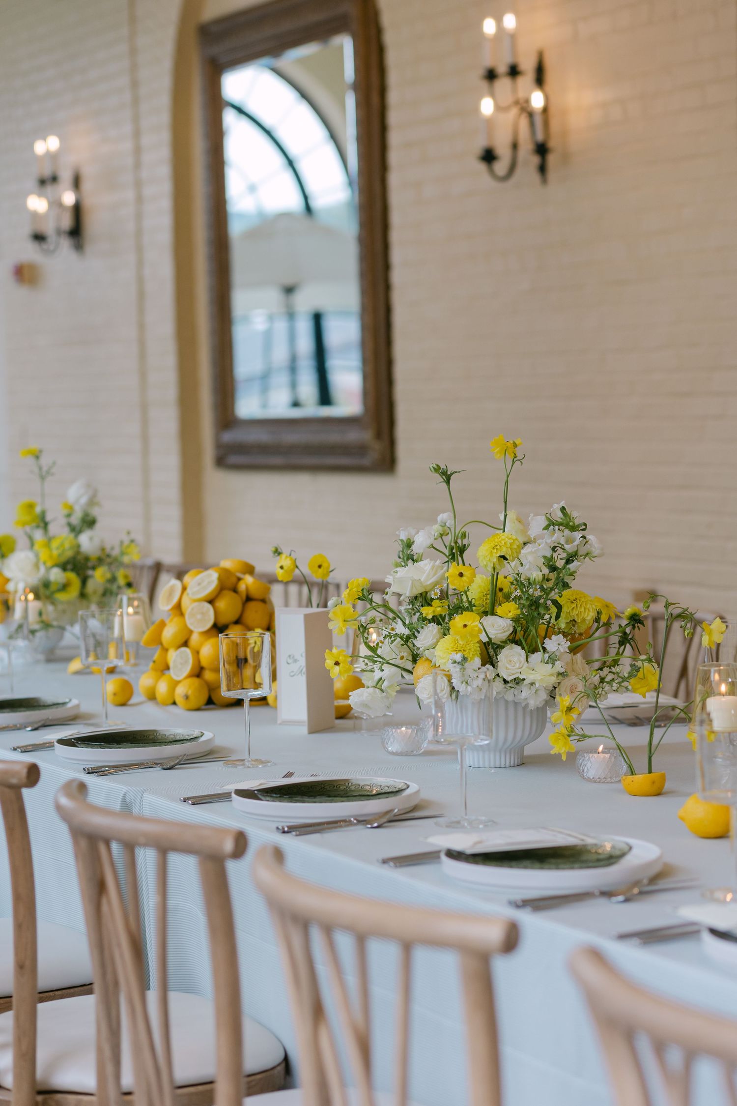 Elegant lemon-themed wedding reception table with yellow floral centerpieces, green plates, and white chairs in a bright venue.
