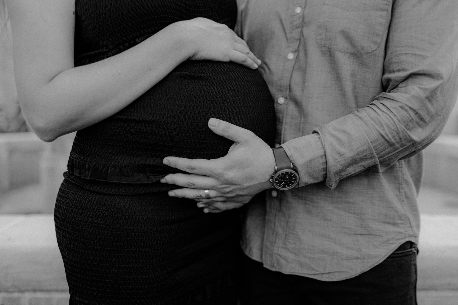 Close up black and white photo of hands resting on a pregnant belly.
