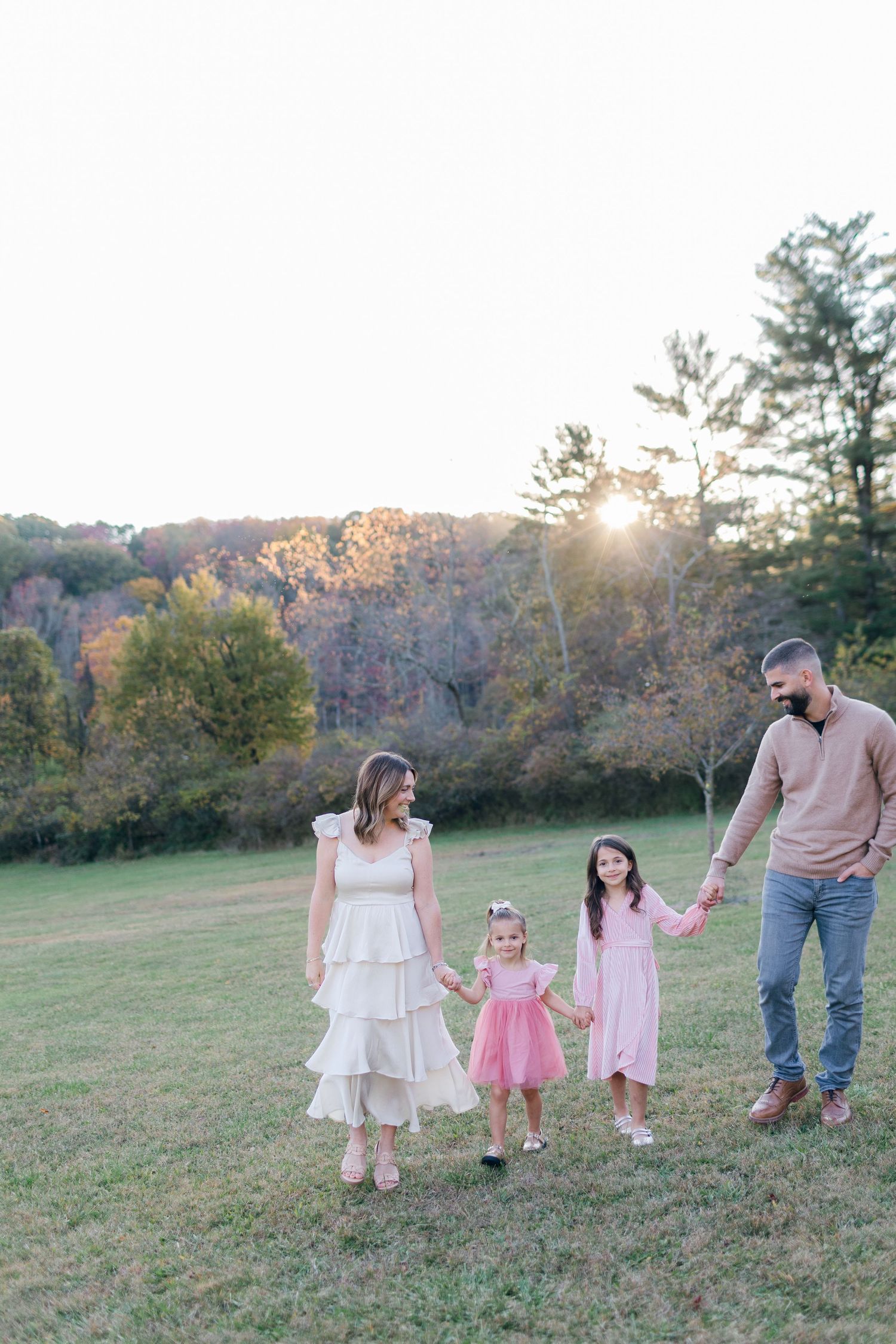 A family walking through a scenic field at sunset with autumn foliage in background.