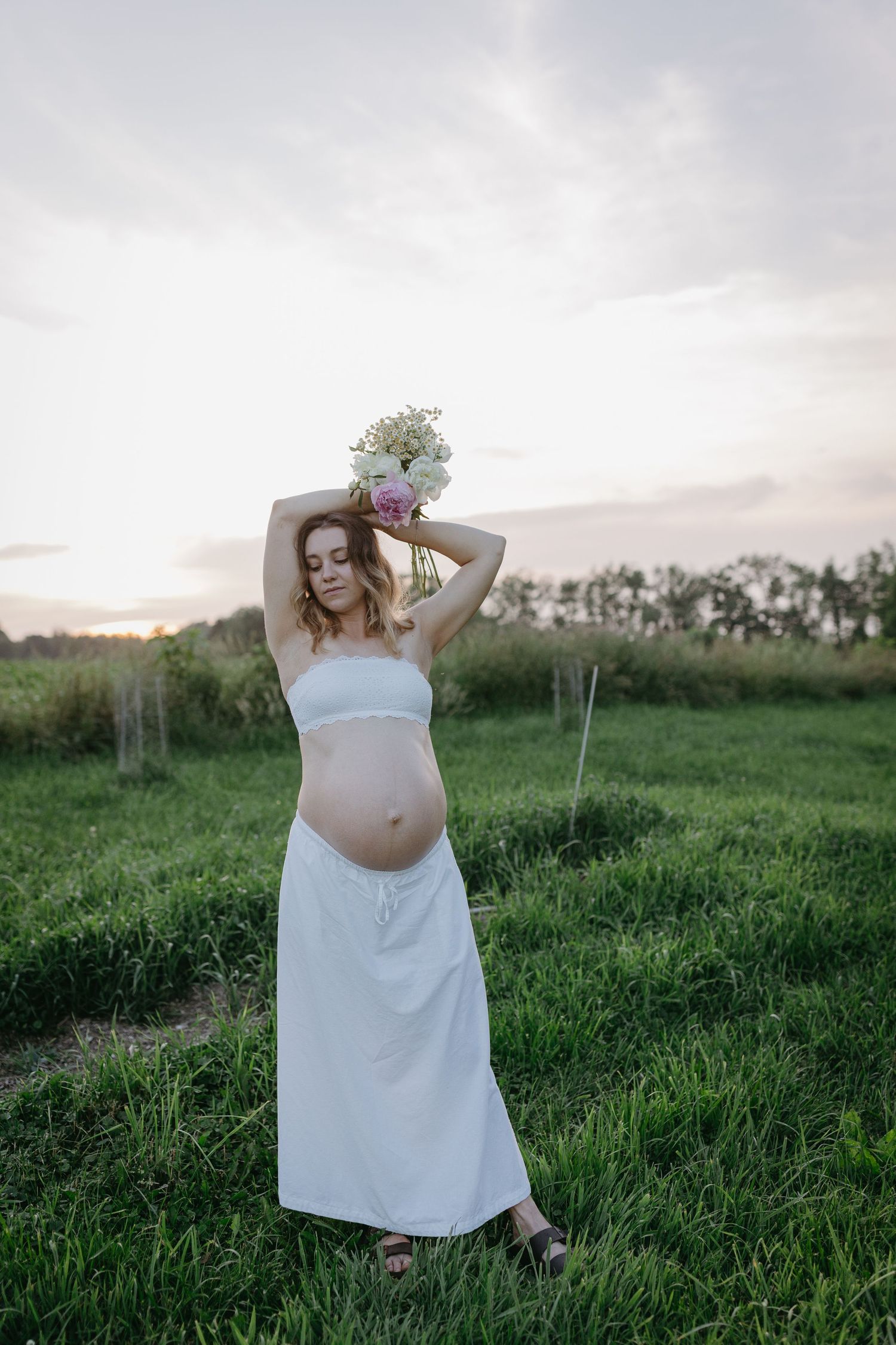 Person in a flowing white dress poses gracefully in a lush green meadow at sunset.