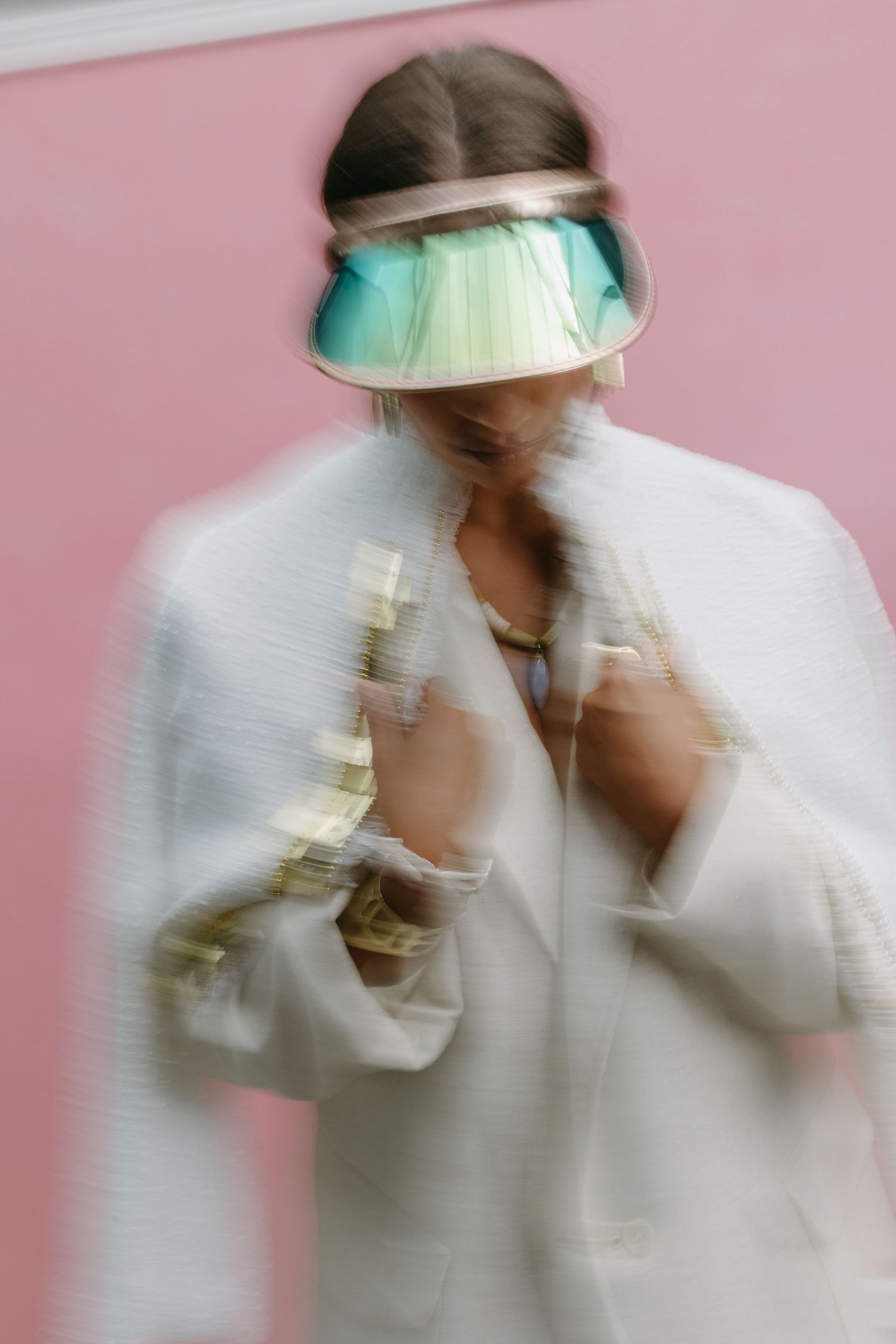Motion blurred figure in white coat and teal medical visor against pink background shows protective pandemic equipment wear.