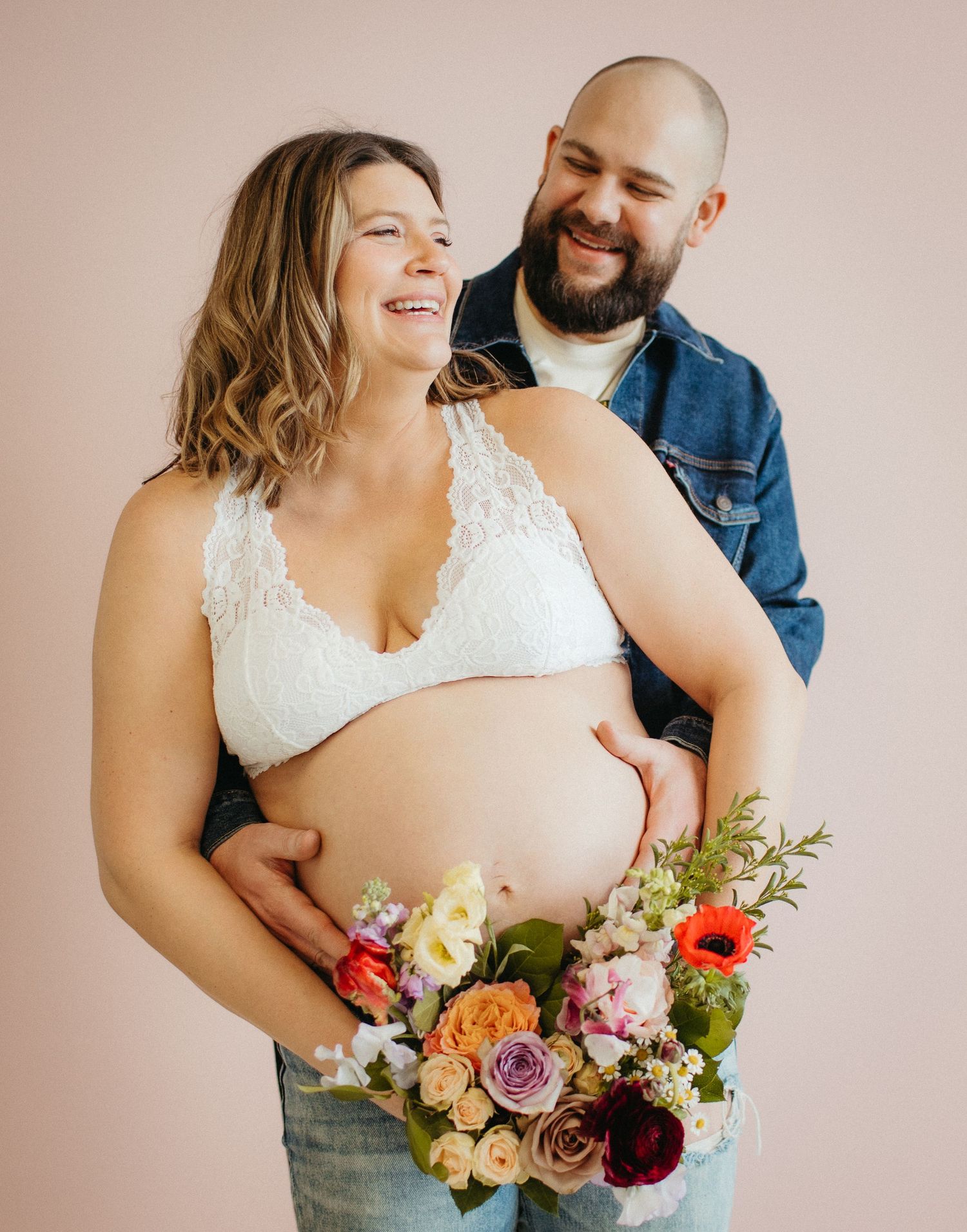 An intimate maternity portrait featuring a beautiful floral bouquet against a pink backdrop.