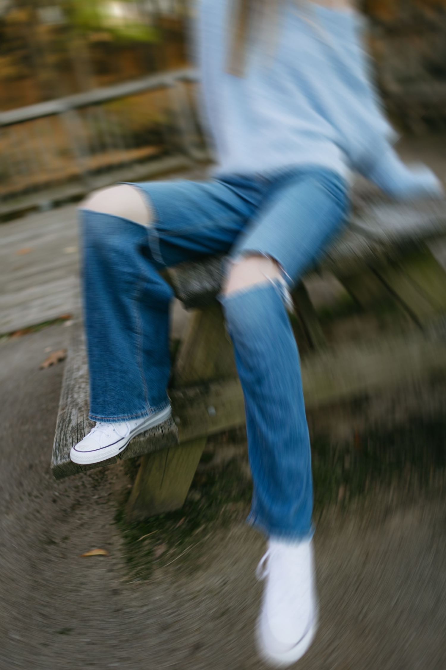 Motion-blurred image of ripped jeans and white sneakers on wooden bench.