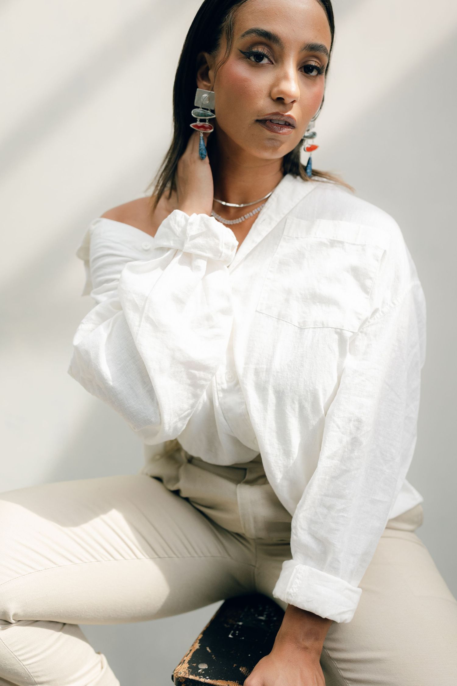 Fashion portrait of woman wearing white button-down shirt and khaki pants with statement turquoise earrings.