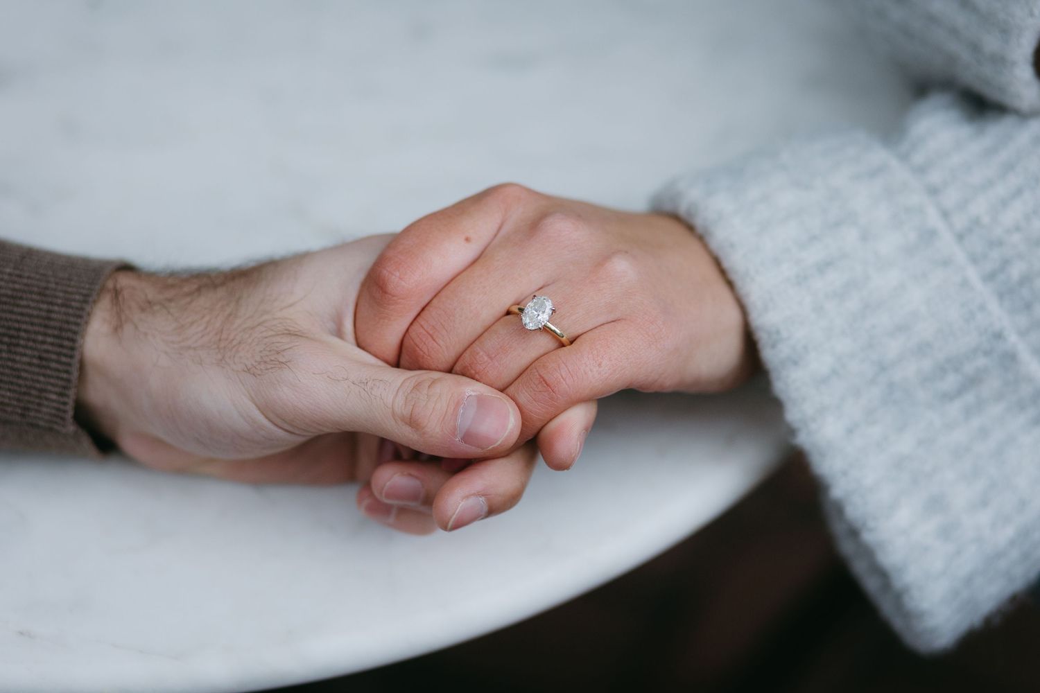 Close-up shot of hands holding each other with an engagement ring visible.